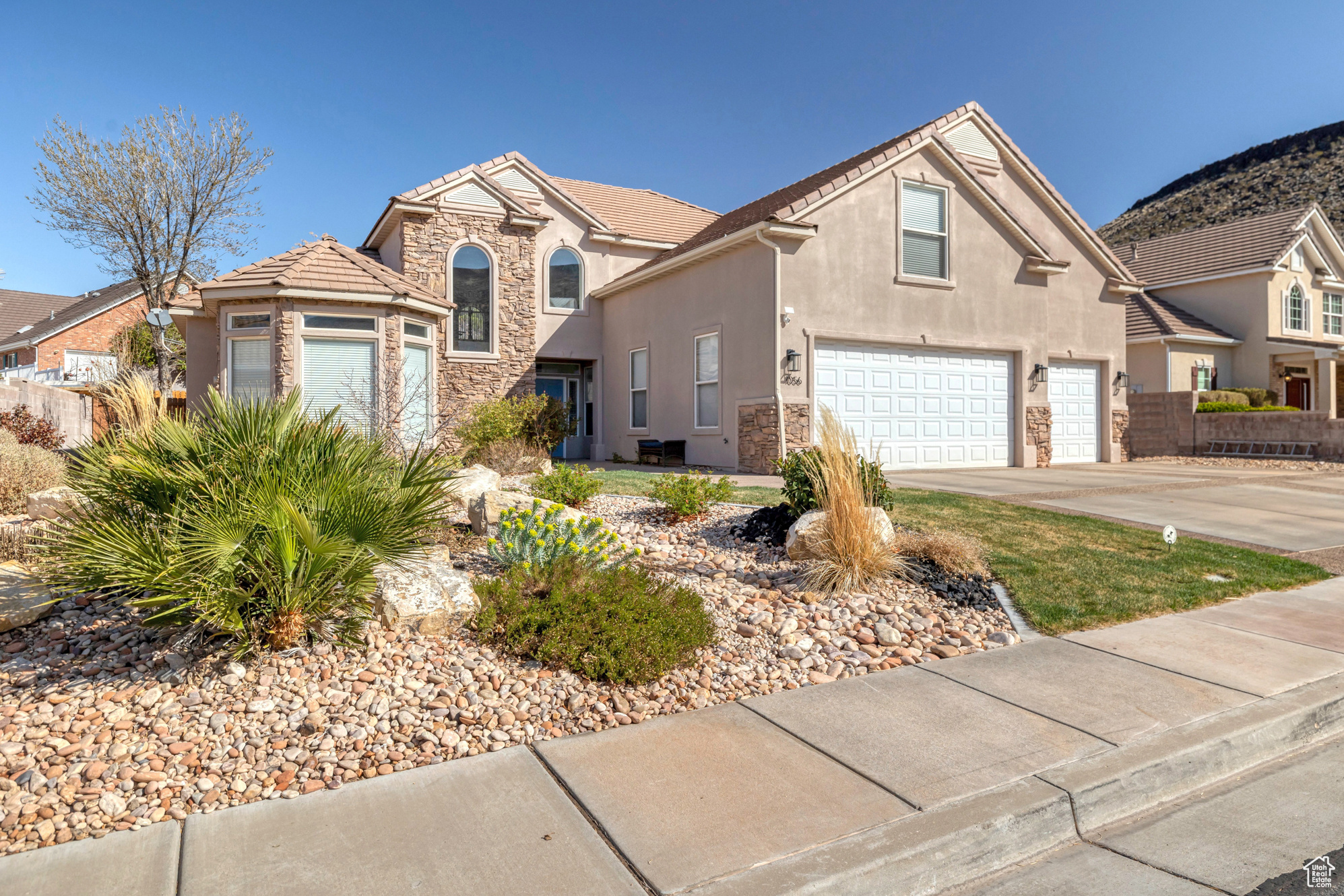 Traditional home featuring a tiled roof, concrete driveway, stucco siding, stone siding, and an attached garage