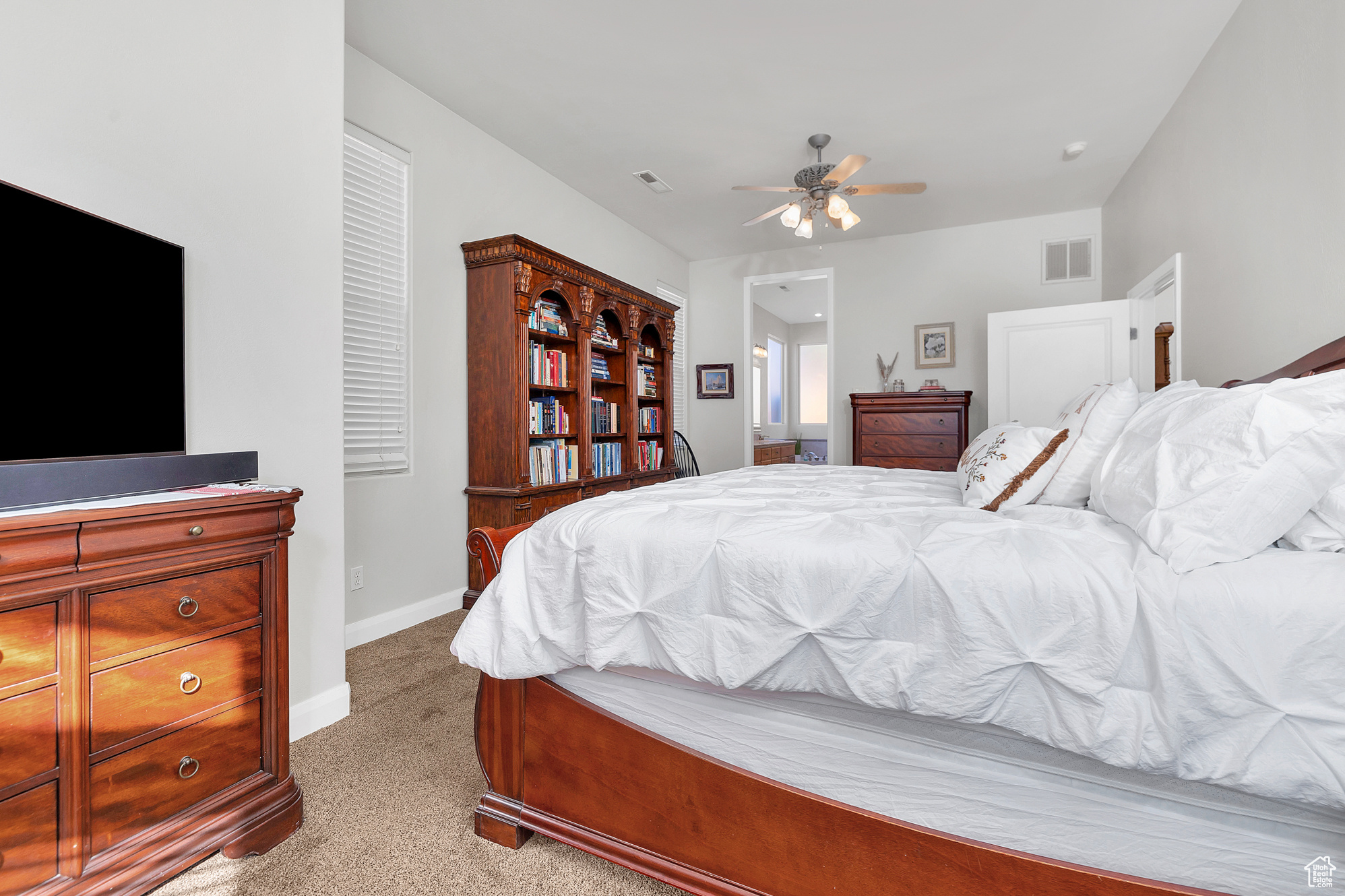 Carpeted bedroom featuring visible vents, baseboards, ensuite bath, and ceiling fan