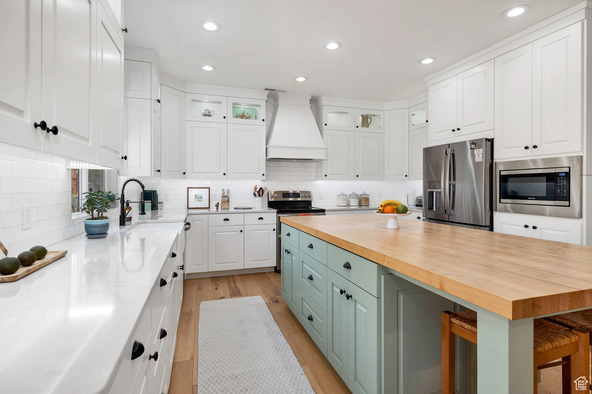 Kitchen with premium range hood, stainless steel appliances, white cabinets, and wood counters