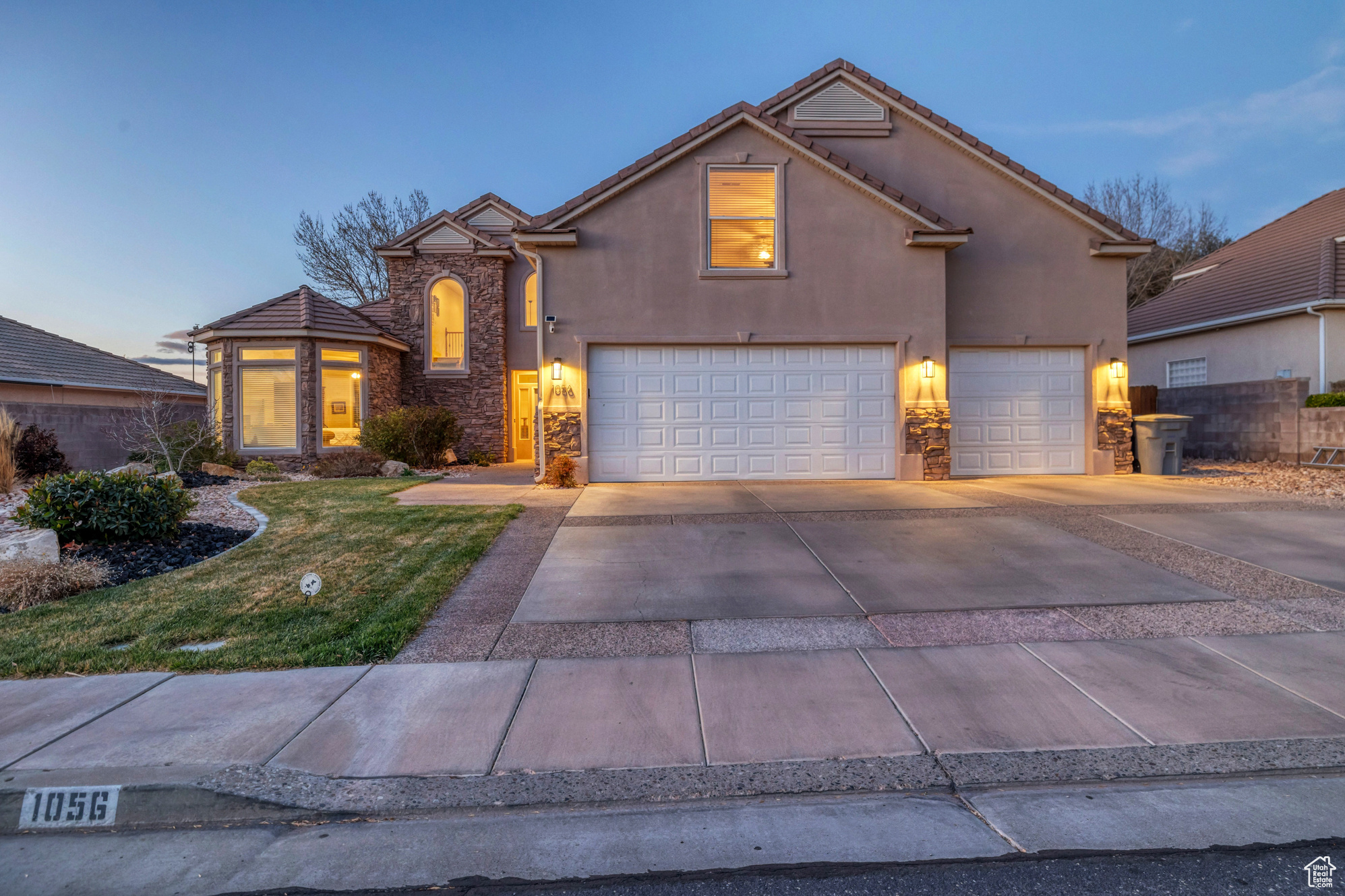 Traditional-style home with stucco siding, driveway, stone siding, fence, and a front yard