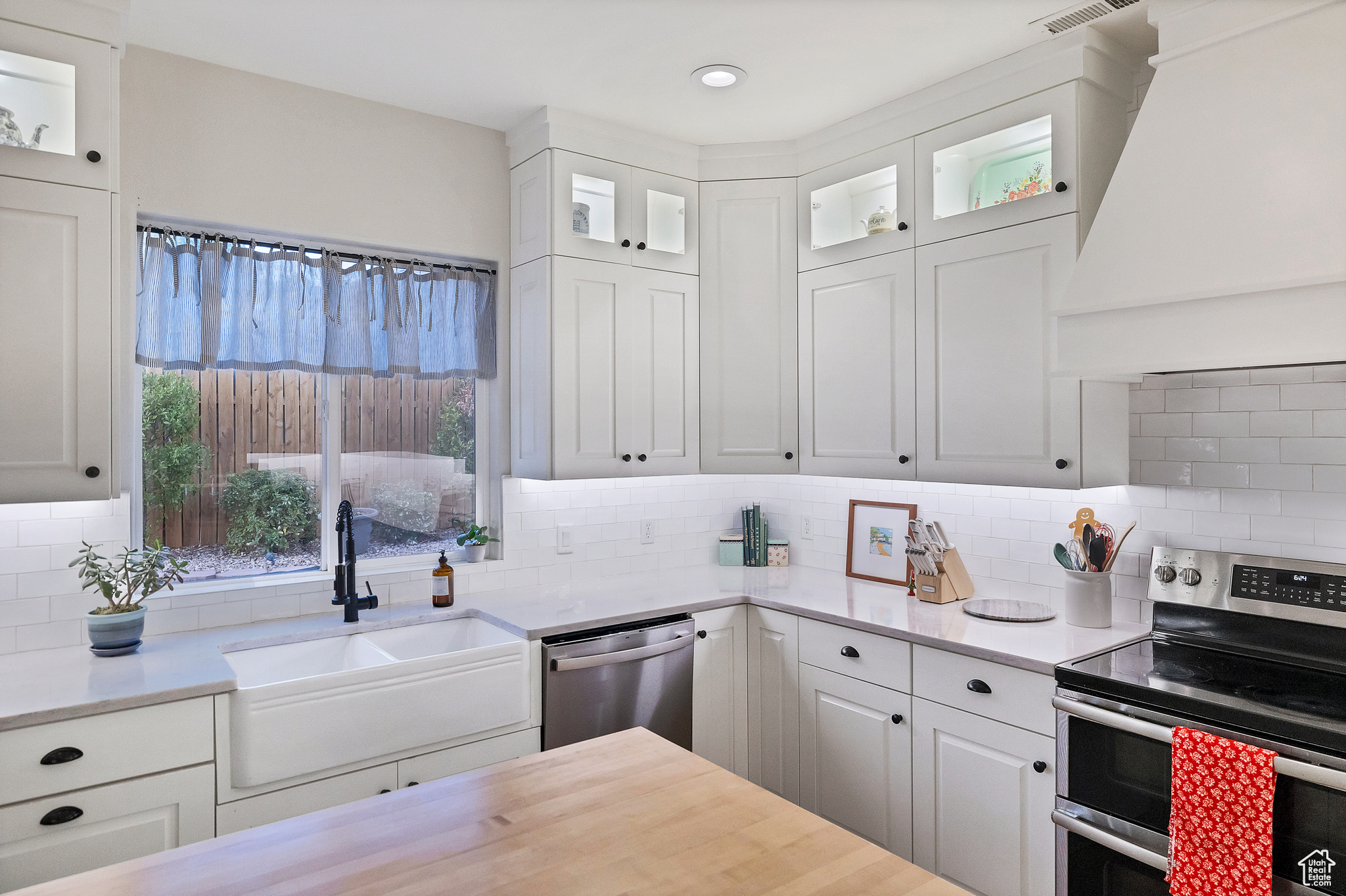 Kitchen featuring decorative backsplash, appliances with stainless steel finishes, custom exhaust hood, white cabinetry, and a sink