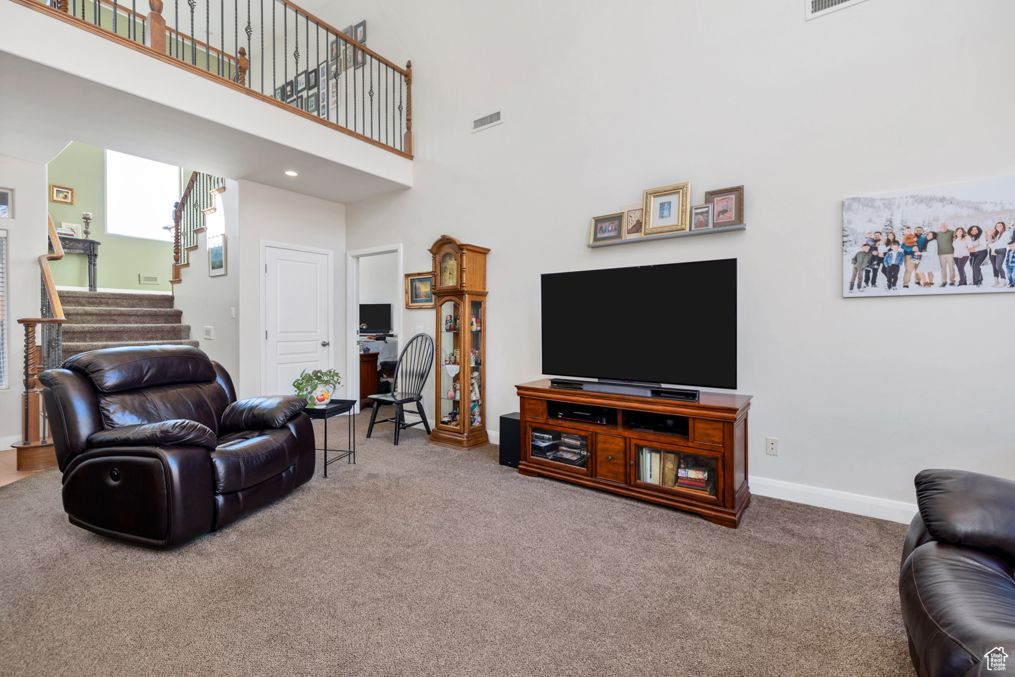 Carpeted living room featuring stairs, a high ceiling, baseboards, and visible vents