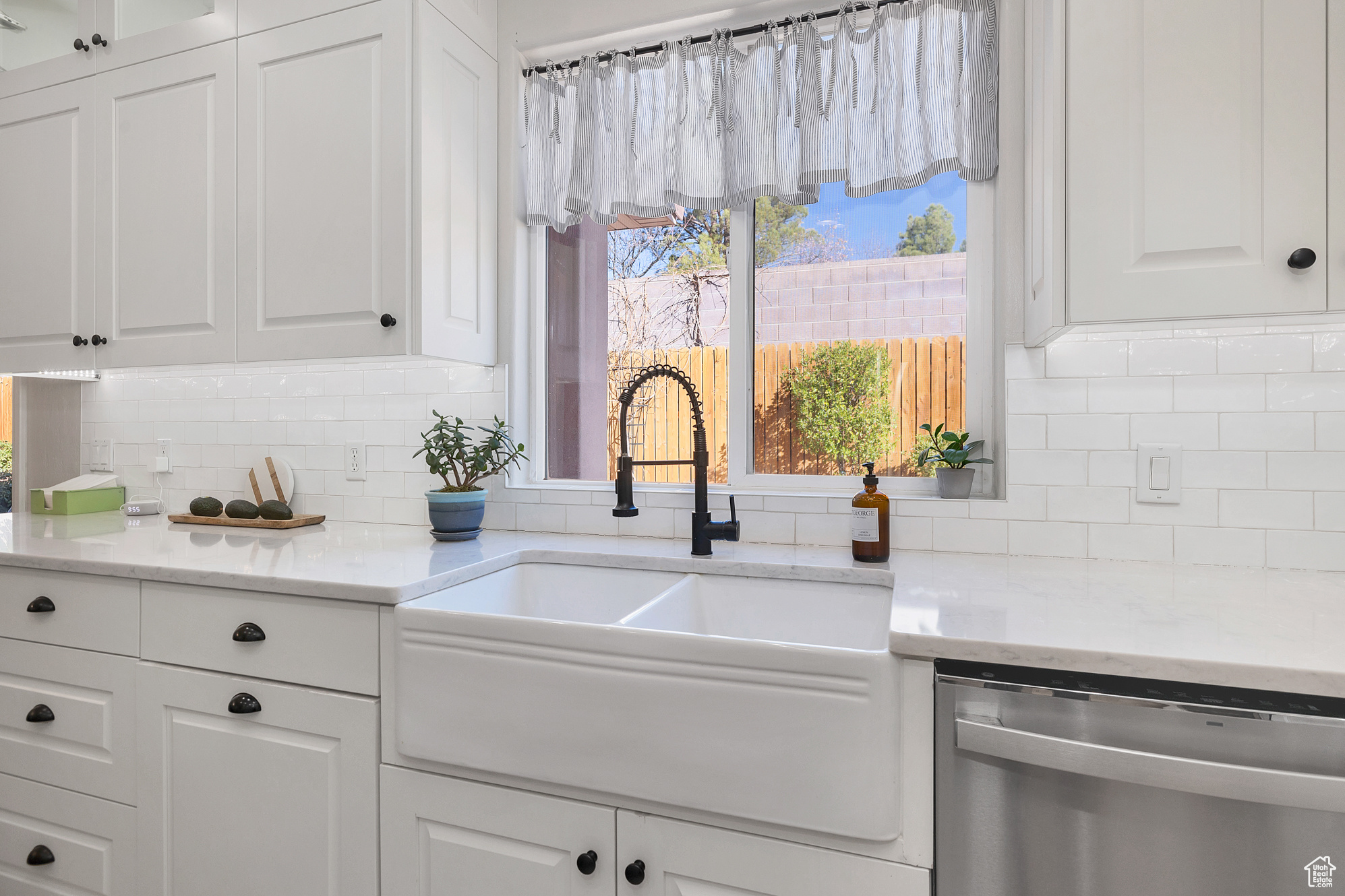 Kitchen with a sink, decorative backsplash, stainless steel dishwasher, and white cabinetry