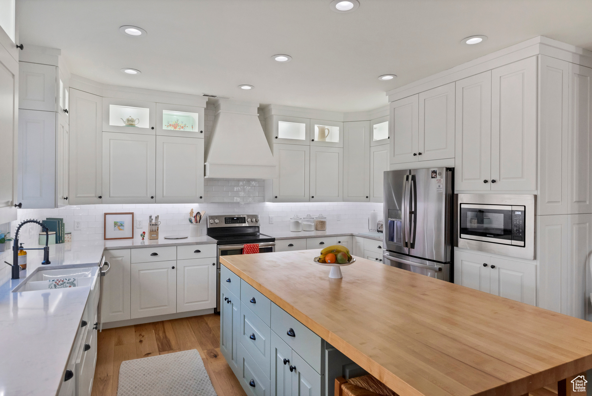Kitchen with a sink, appliances with stainless steel finishes, white cabinets, butcher block counters, and custom exhaust hood