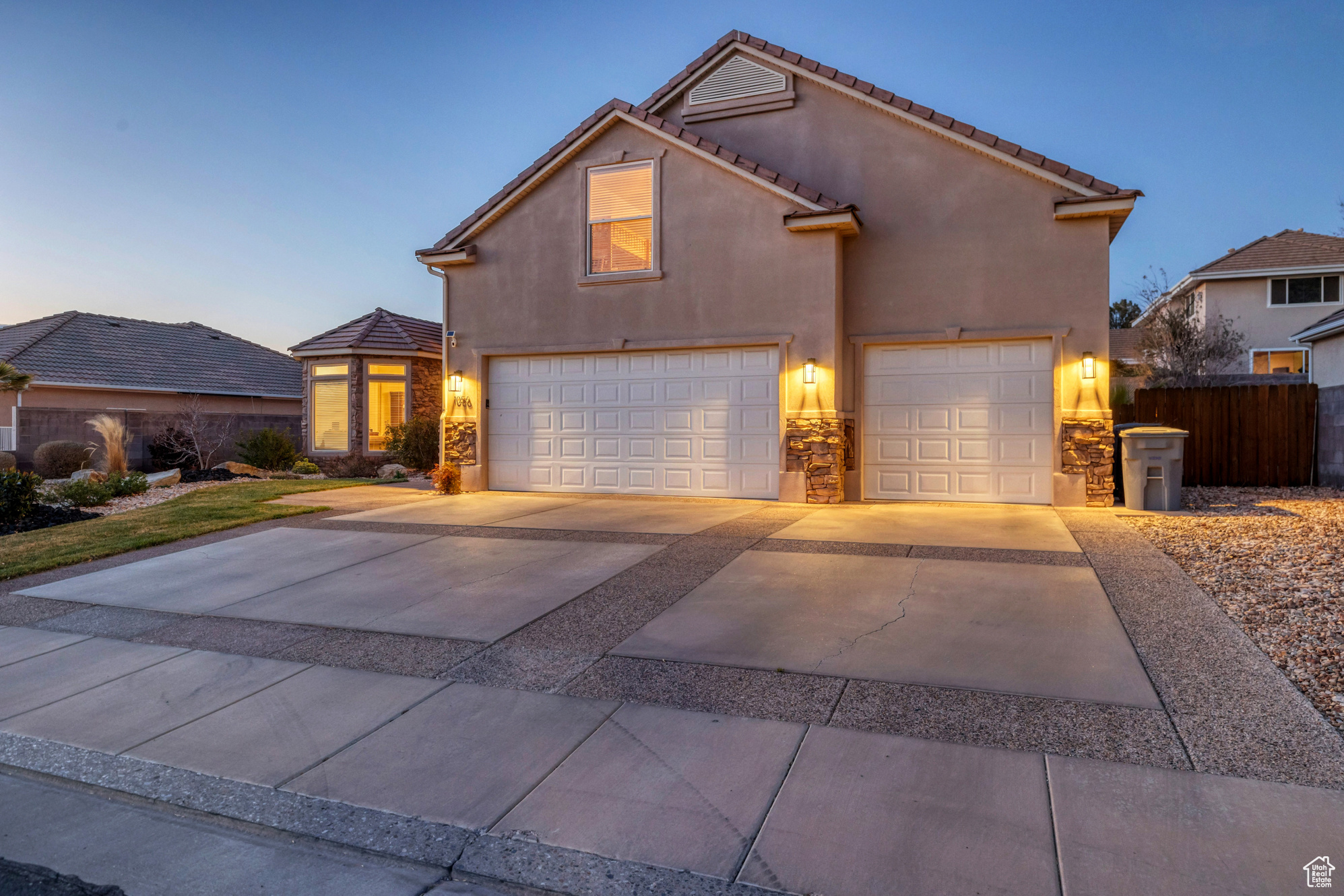 View of front facade with fence, driveway, stucco siding, stone siding, and a tiled roof