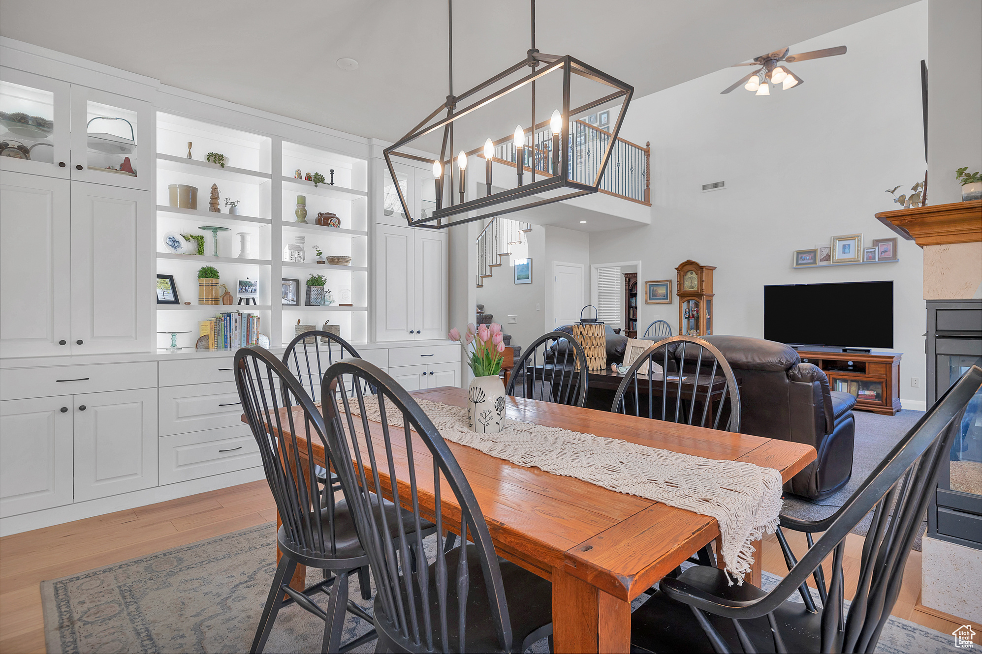 Dining area with stairway, light wood-style flooring, ceiling fan with notable chandelier, and a towering ceiling