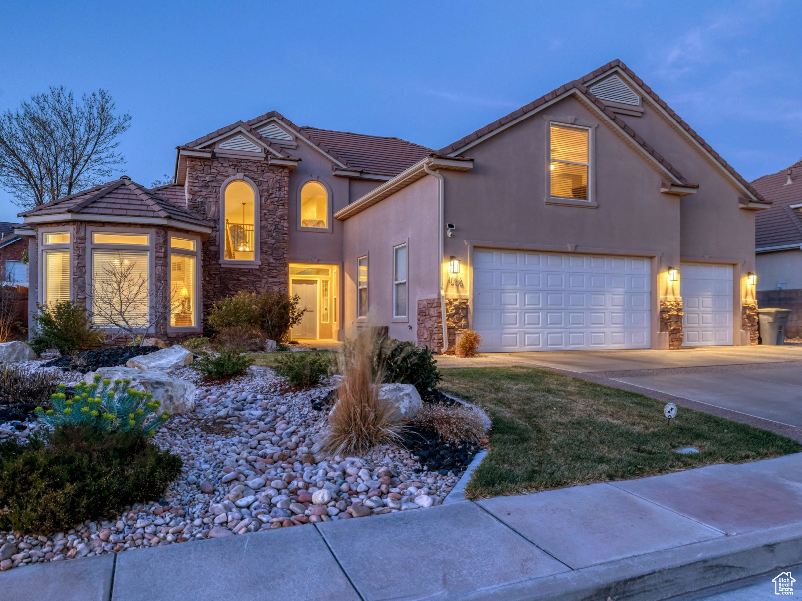 View of front facade featuring stucco siding, driveway, stone siding, fence, and a garage