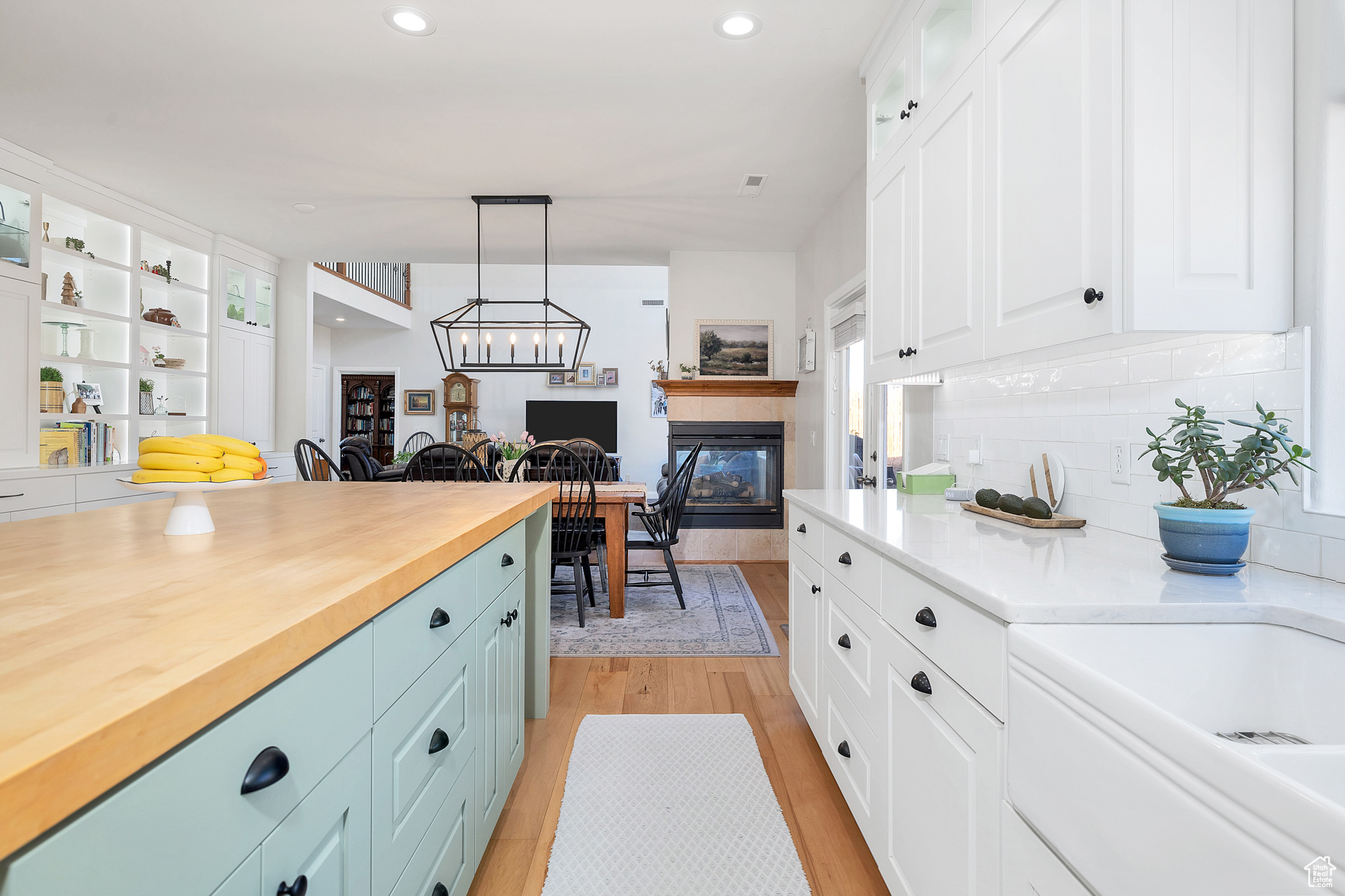 Kitchen featuring a tile fireplace, decorative backsplash, white cabinets, glass insert cabinets, and light wood-style floors