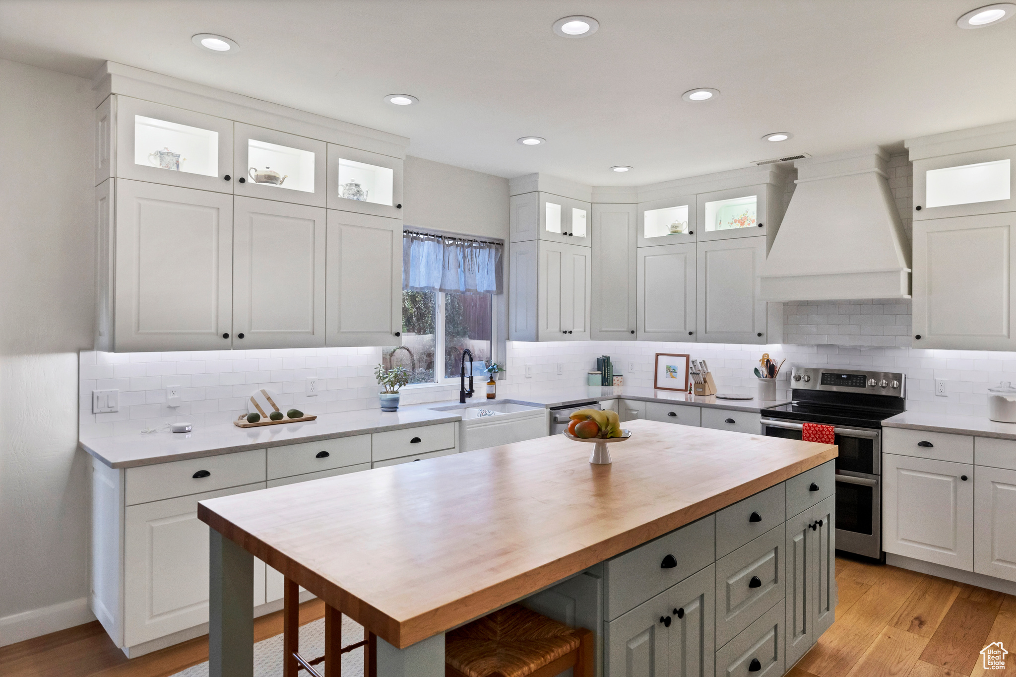 Kitchen featuring premium range hood, light wood-style flooring, a sink, white cabinetry, and appliances with stainless steel finishes