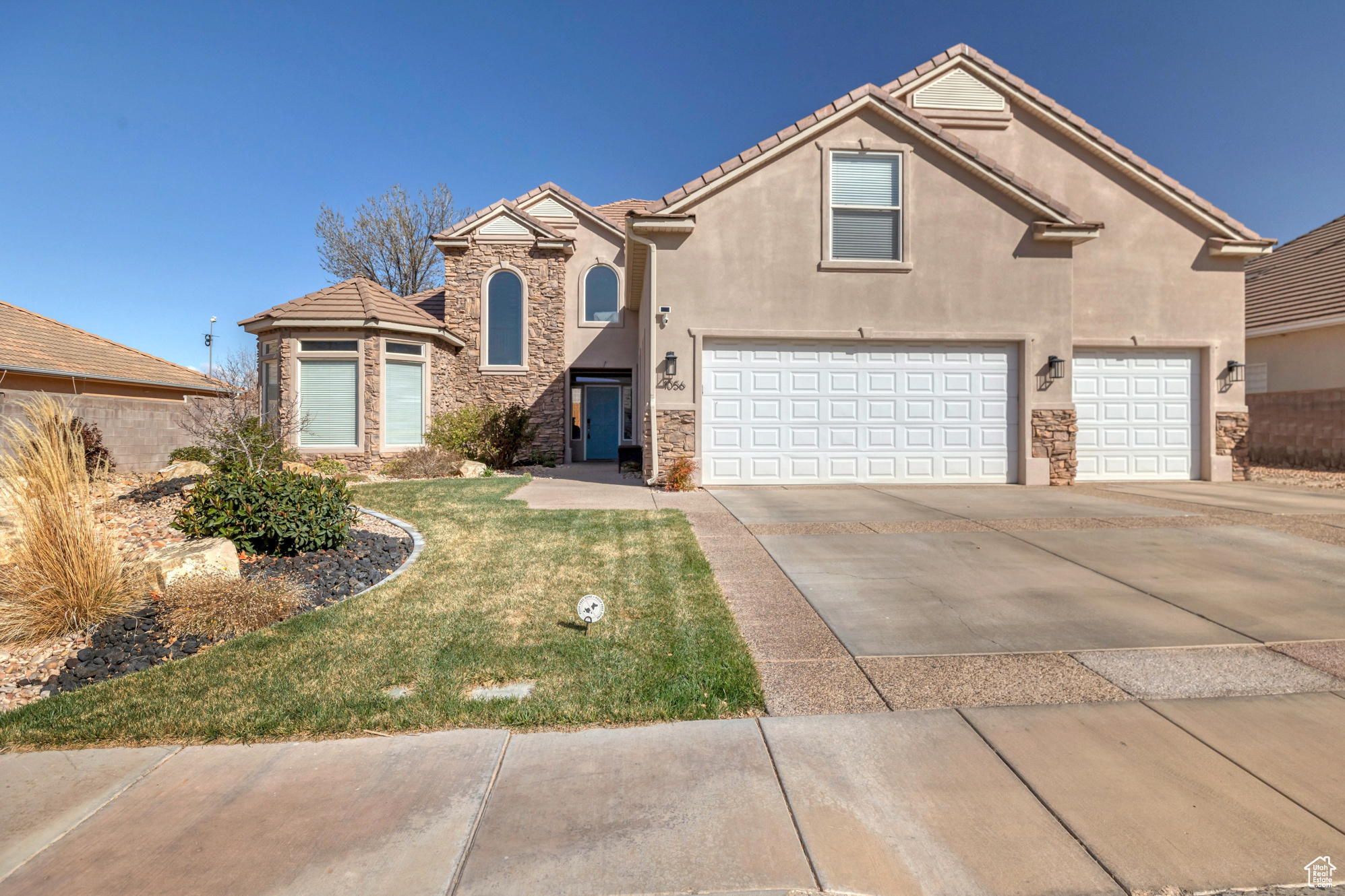 View of front of home featuring stucco siding, a front lawn, driveway, stone siding, and an attached garage