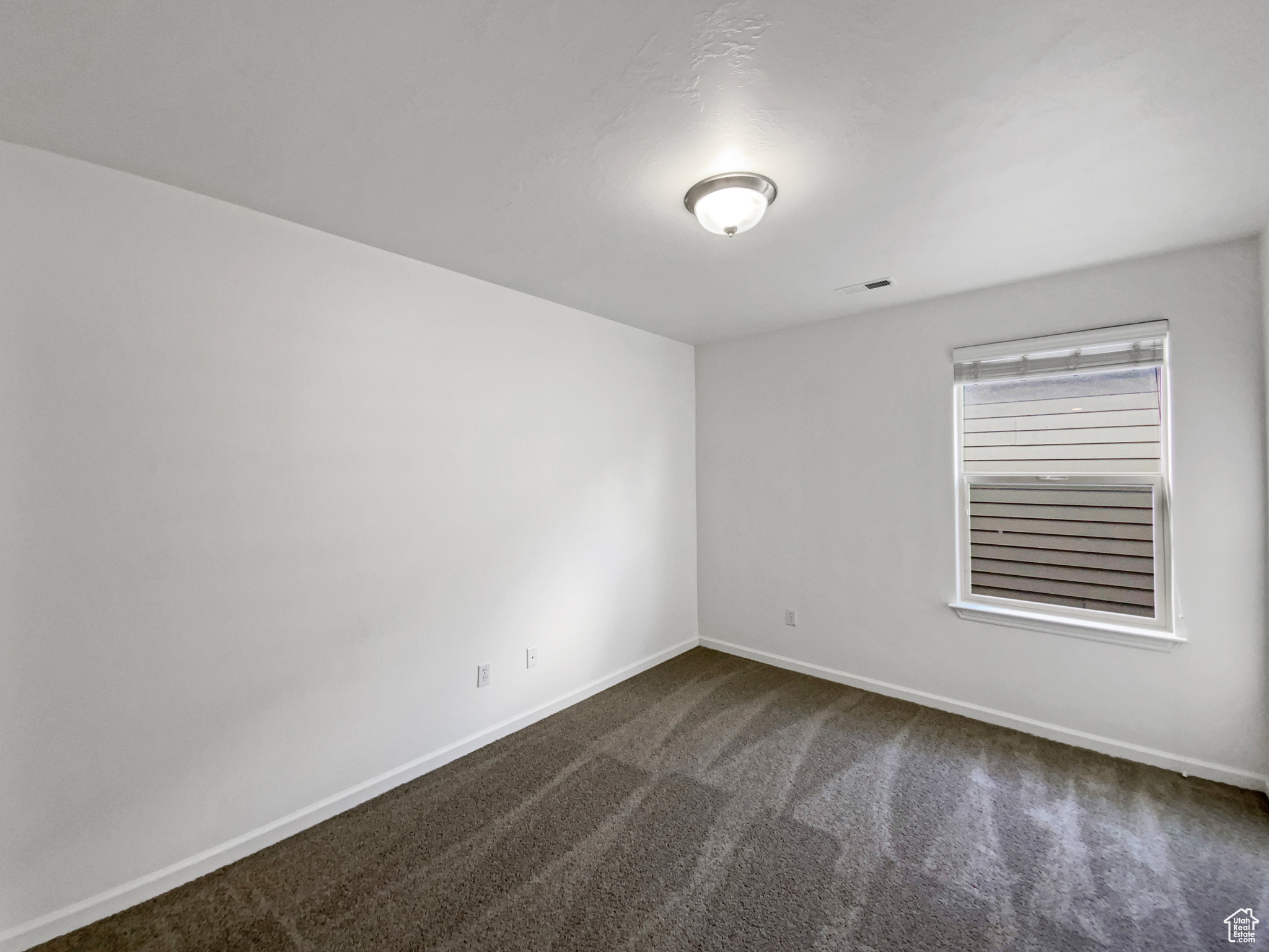 Unfurnished room with dark colored carpet, visible vents, and baseboards