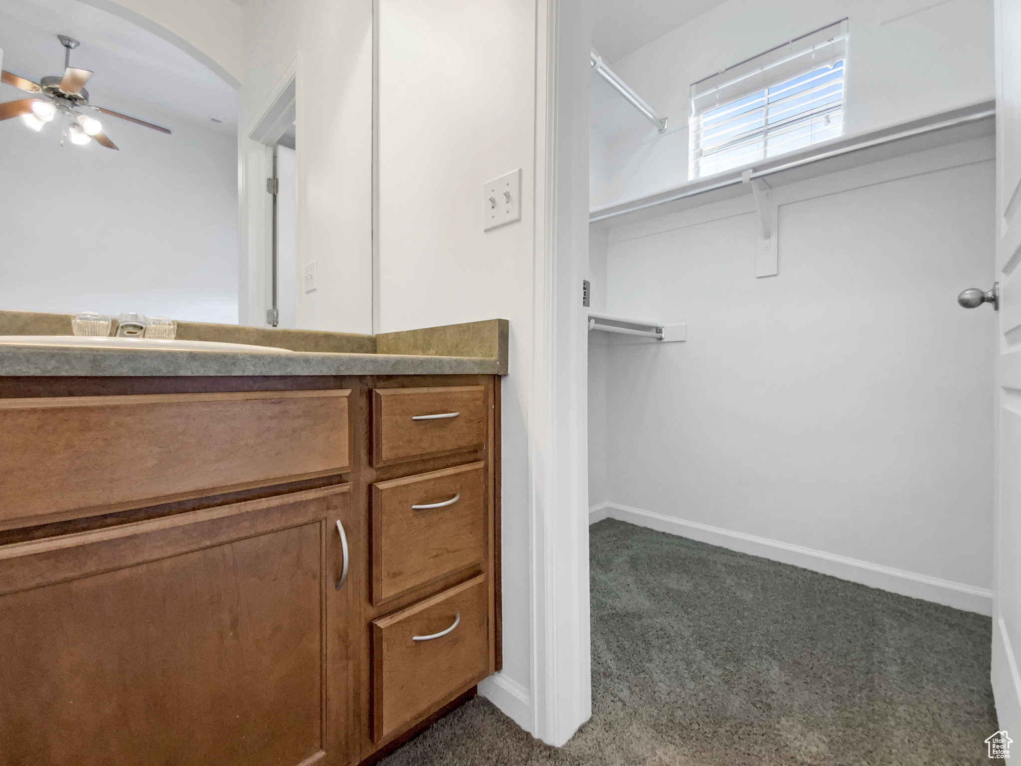 Spacious closet featuring a sink, arched walkways, dark carpet, and ceiling fan