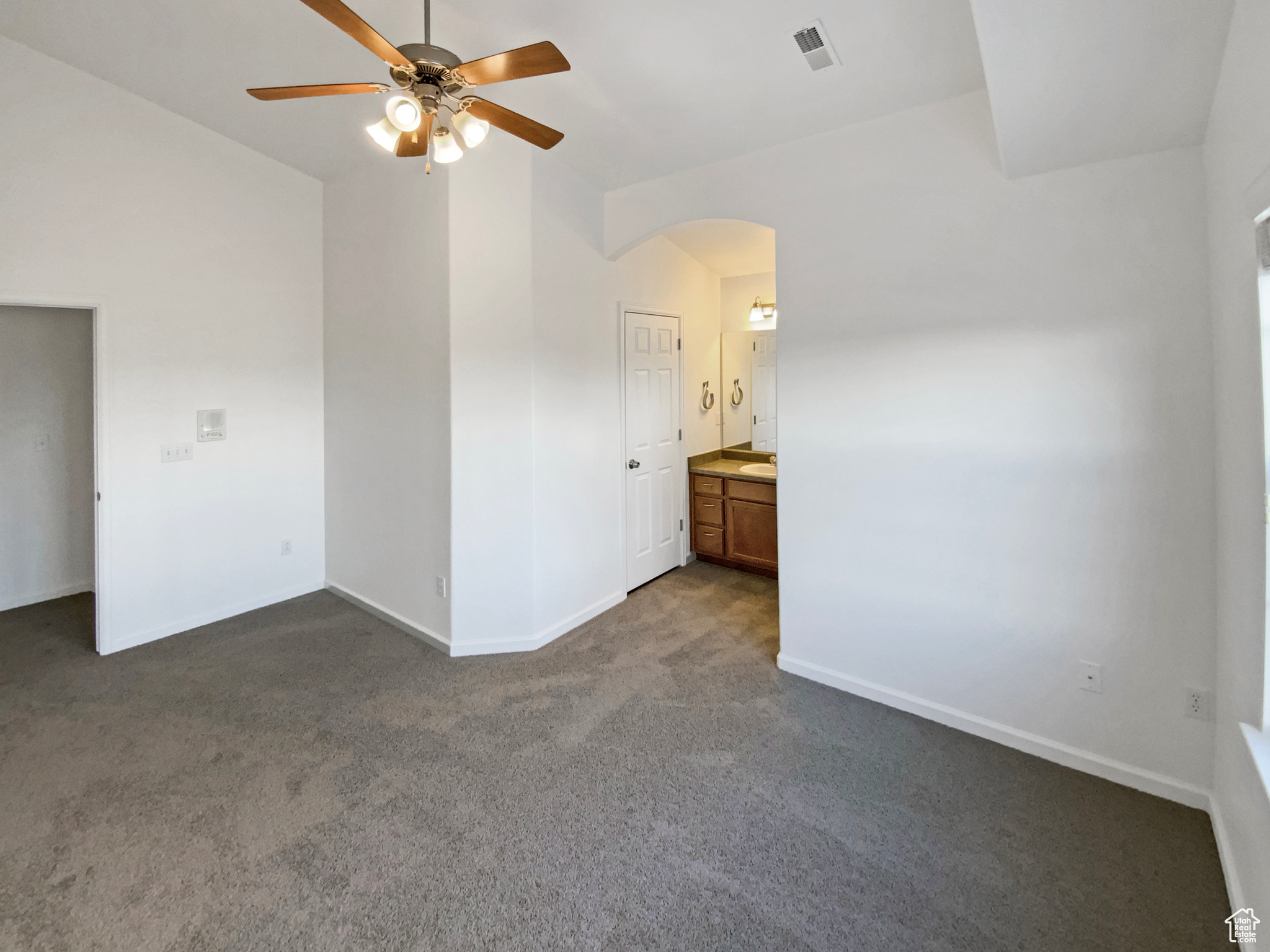 Empty room featuring visible vents, arched walkways, dark colored carpet, baseboards, and ceiling fan