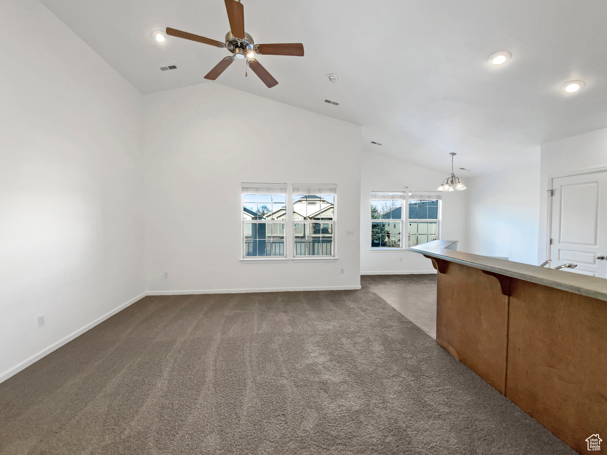 Unfurnished living room with visible vents, baseboards, lofted ceiling, ceiling fan with notable chandelier, and dark colored carpet