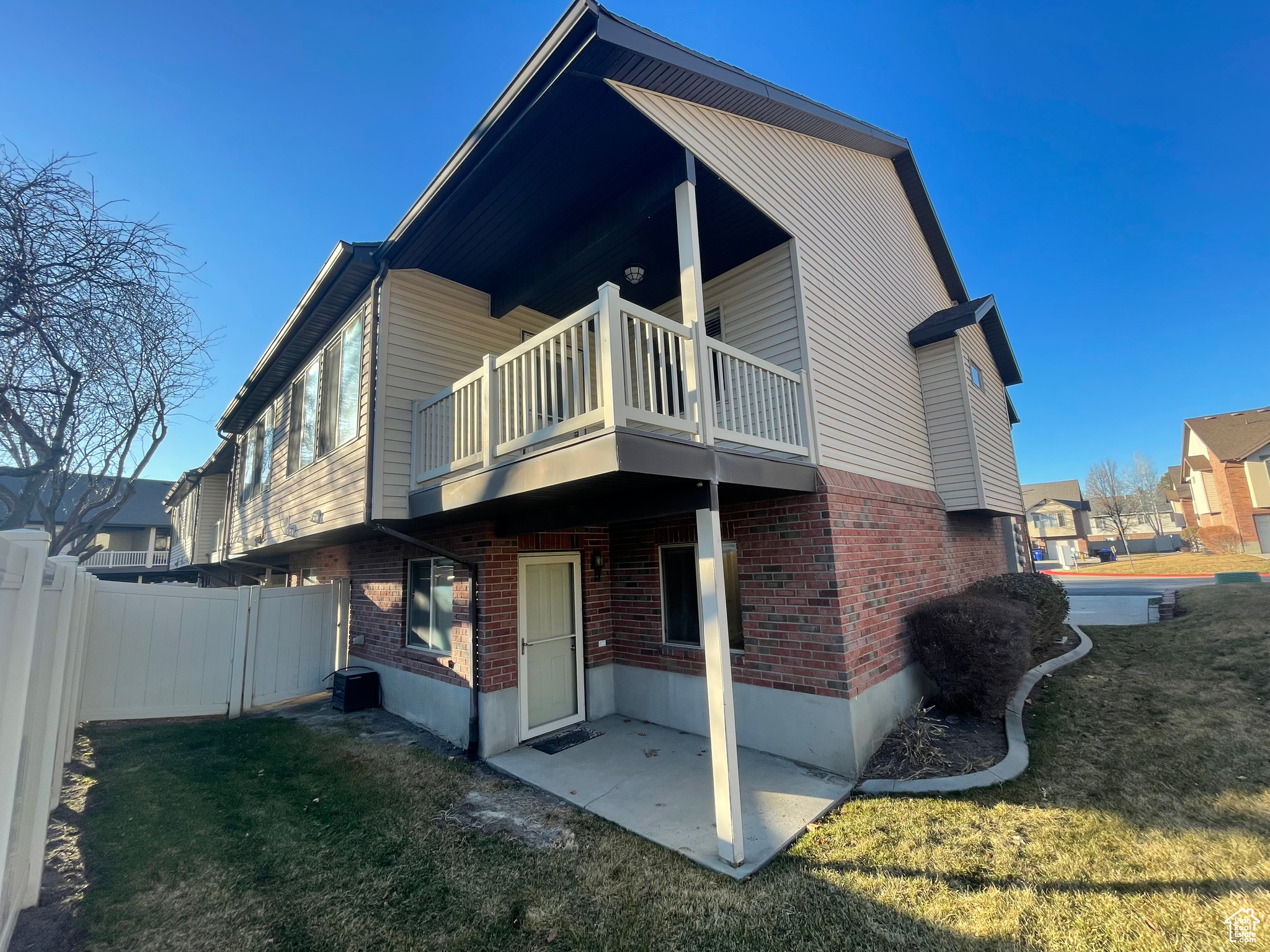 Back of property featuring a covered patio, covered balcony, brick siding, lawn and fence