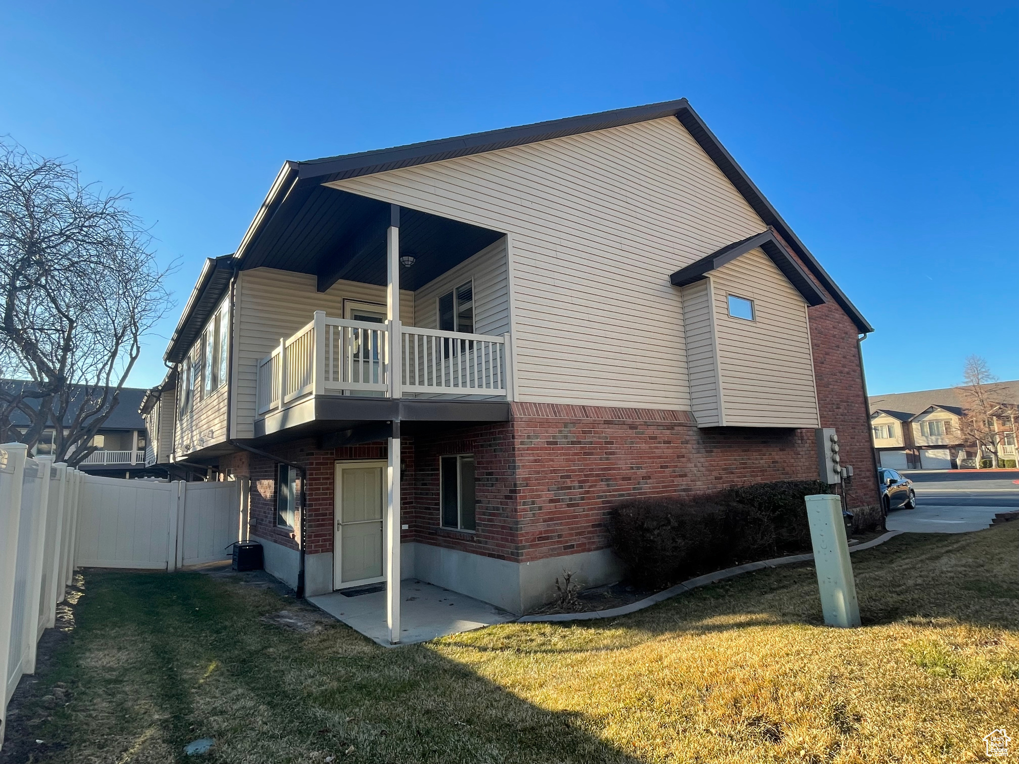 View of property exterior featuring a balcony, a yard, a fenced backyard, and brick siding