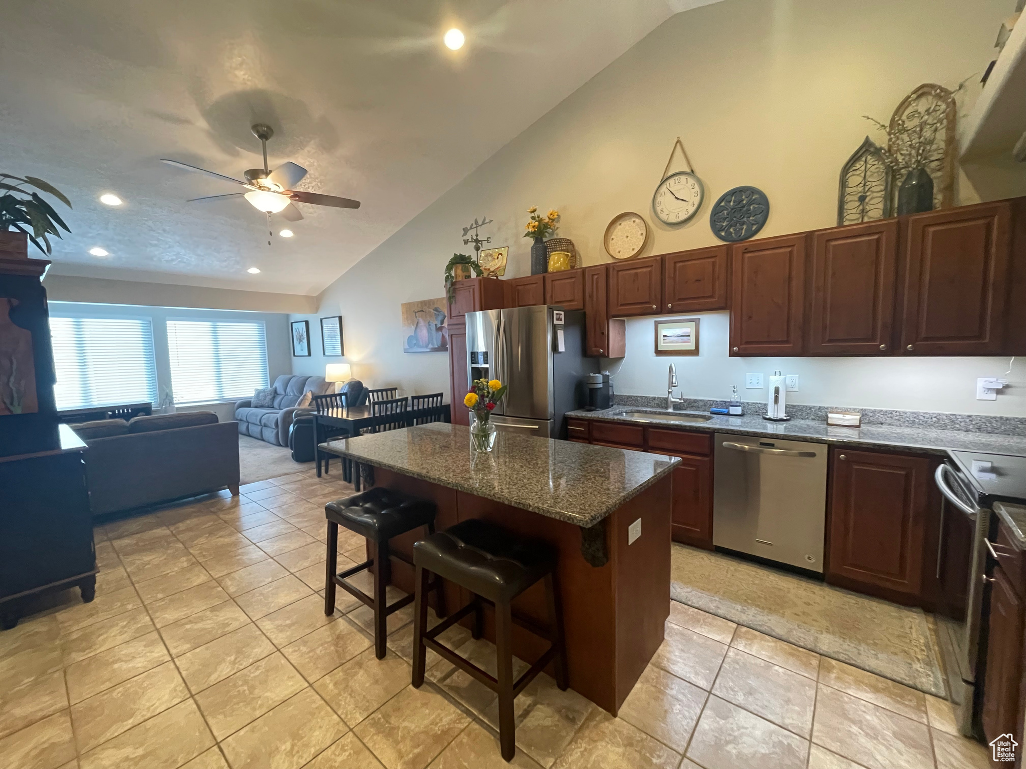 Kitchen with light tile floors, stainless steel refrigerator with ice dispenser, a vaulted textured ceiling, a kitchen bar, and open floor plan
