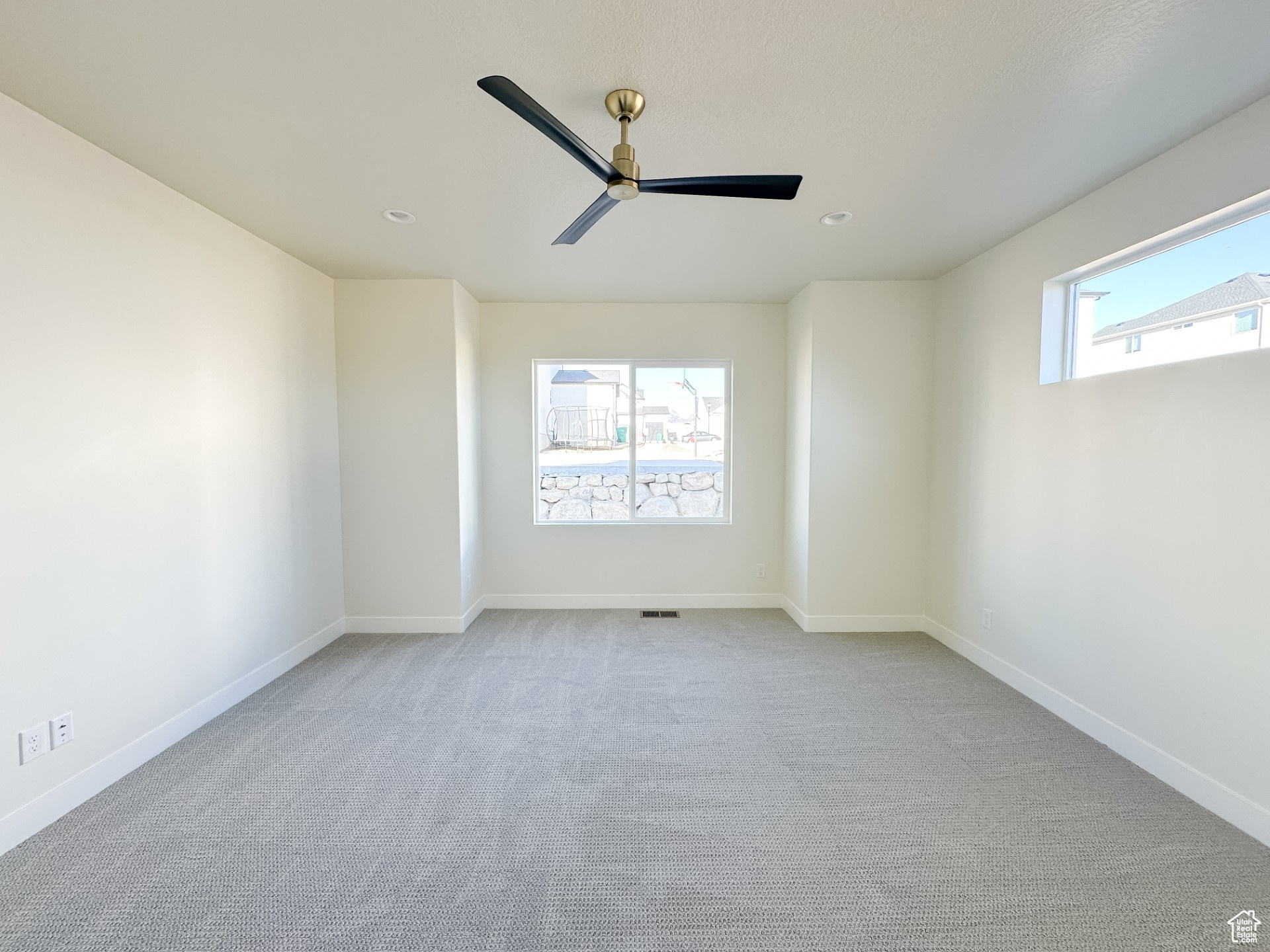 Carpeted spare room with visible vents, a healthy amount of sunlight, baseboards, and ceiling fan