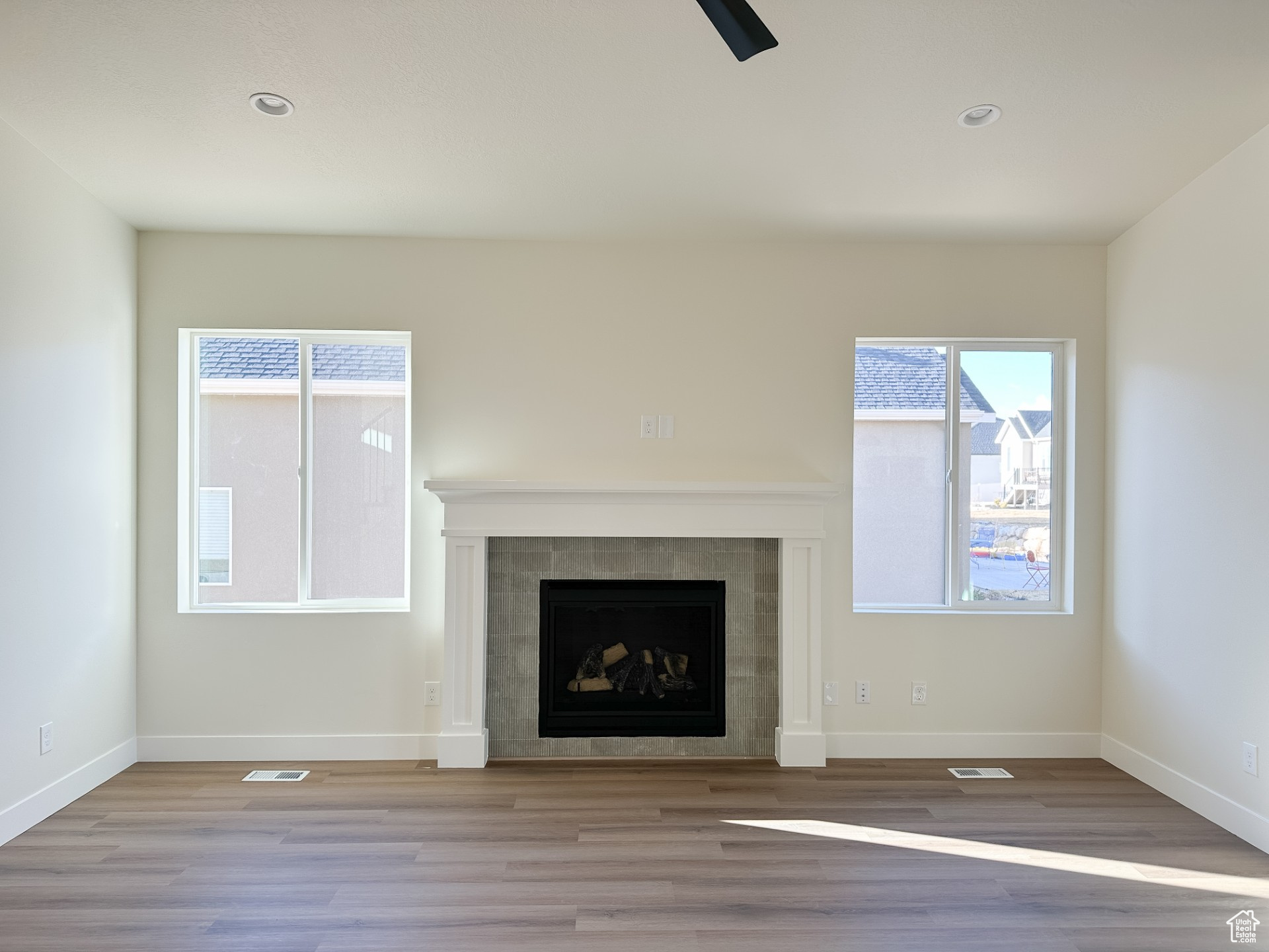 Unfurnished living room with a tiled fireplace, wood finished floors, baseboards, and a wealth of natural light