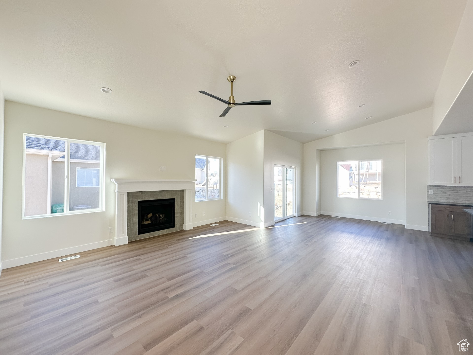 Unfurnished living room with ceiling fan, baseboards, vaulted ceiling, a tile fireplace, and light wood-style floors