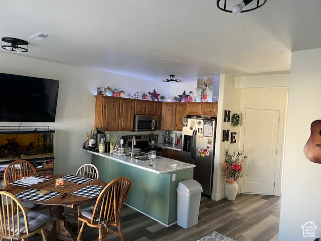 Kitchen with light countertops, appliances with stainless steel finishes, a peninsula, wood finished floors, and a sink