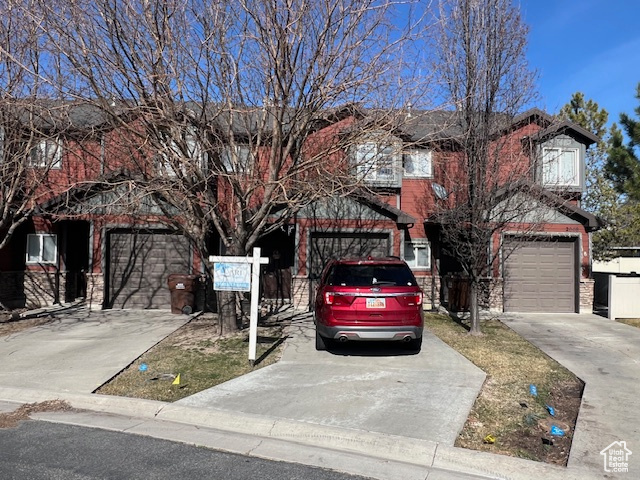 View of property with a garage, brick siding, and driveway