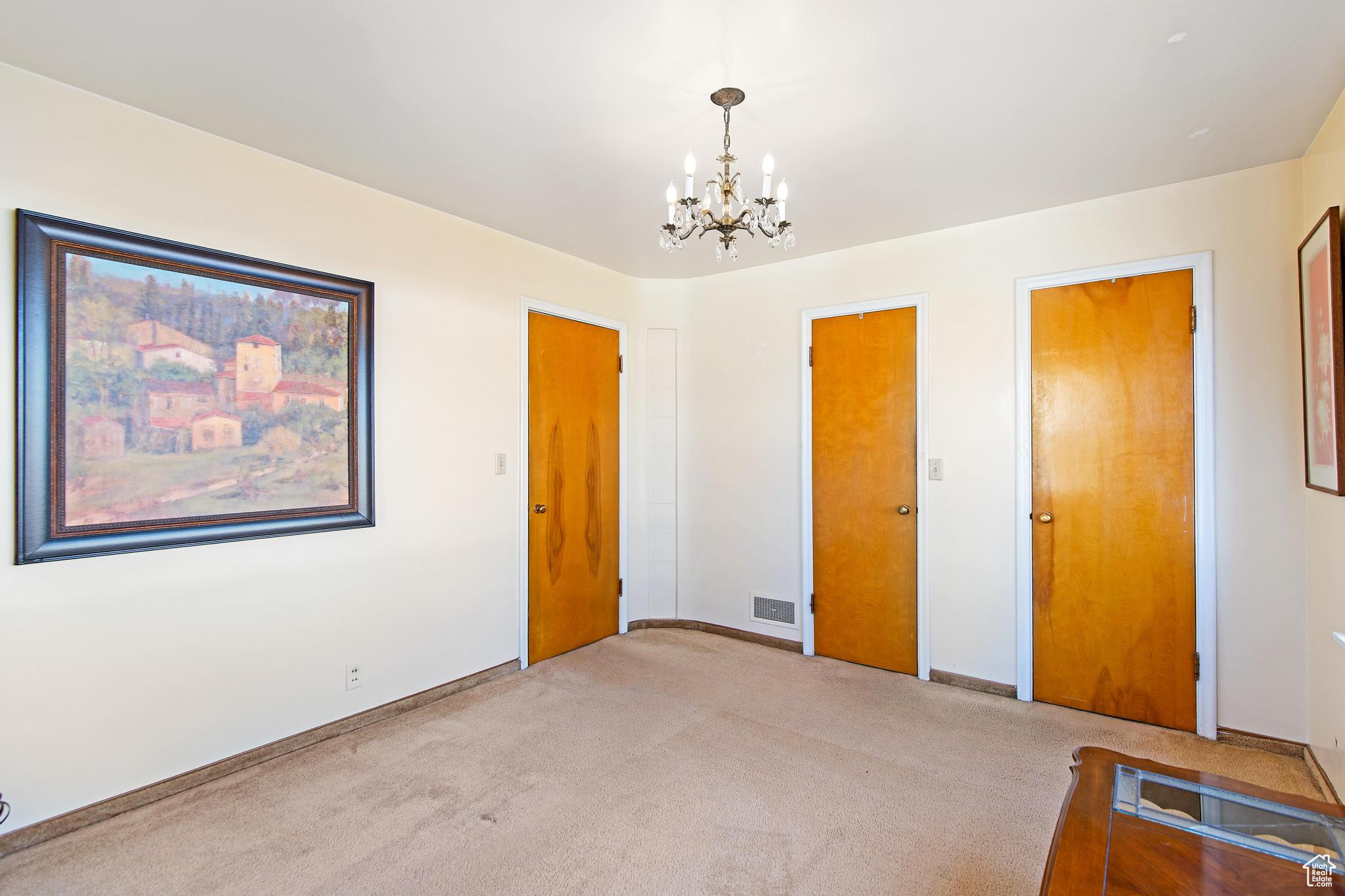 Unfurnished bedroom with light carpet, visible vents, baseboards, and an inviting chandelier