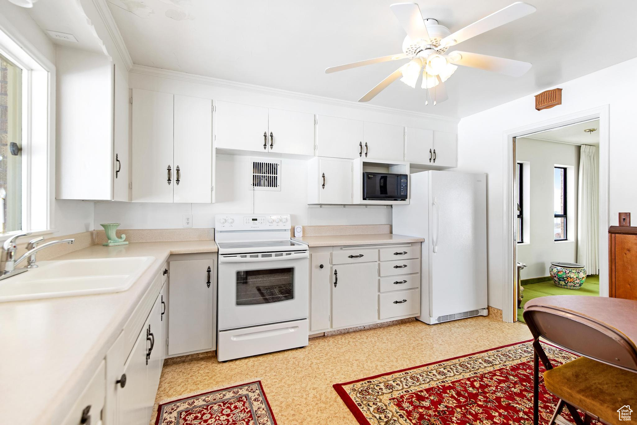 Kitchen featuring visible vents, light countertops, white appliances, white cabinetry, and a sink
