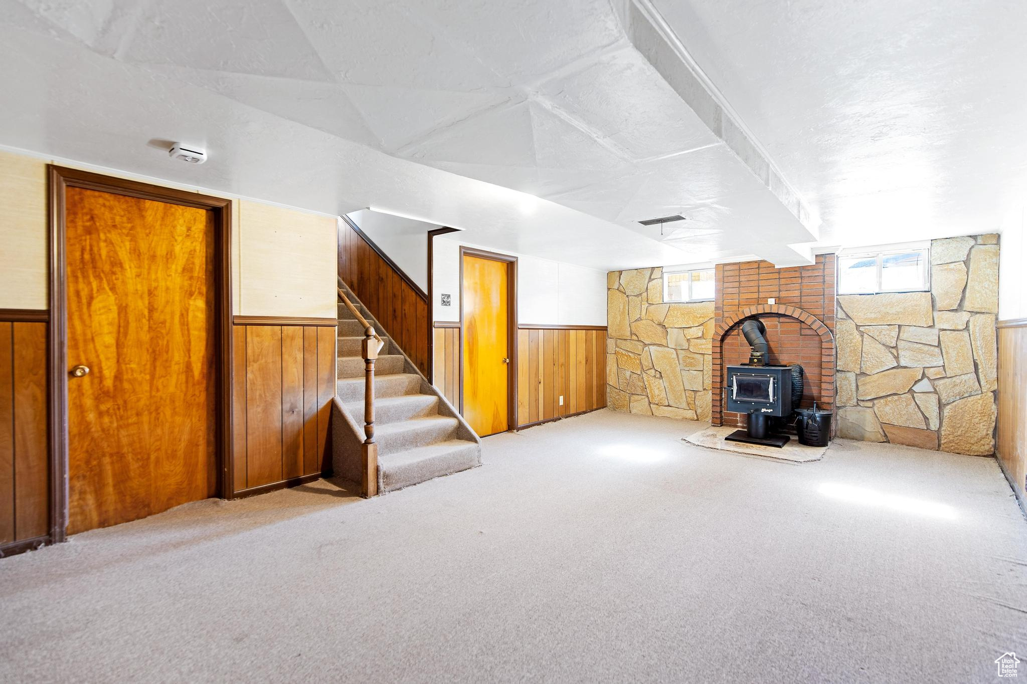 Additional living space featuring a wainscoted wall, wooden walls, a wood stove, and stairway