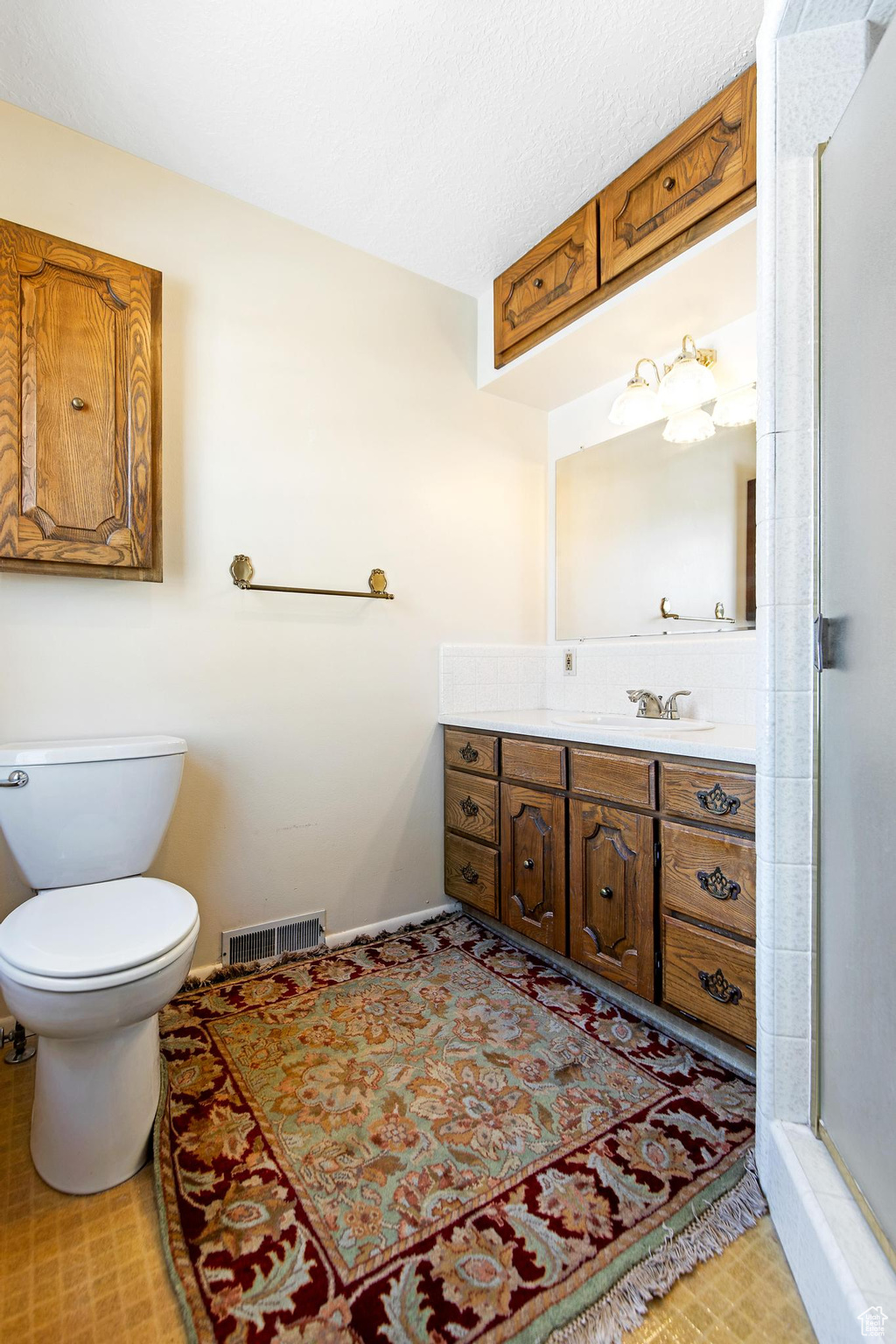 Bathroom with a shower with door, visible vents, toilet, and vanity