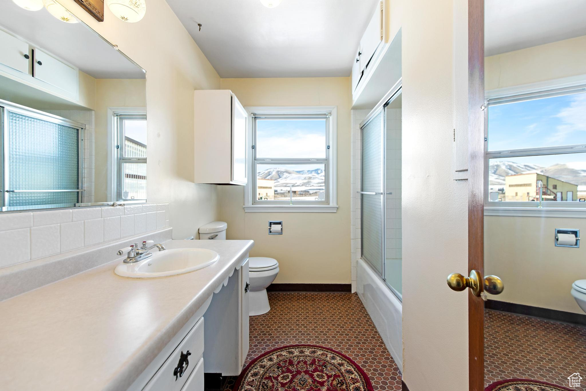 Full bath with combined bath / shower with glass door, toilet, vanity, and baseboards