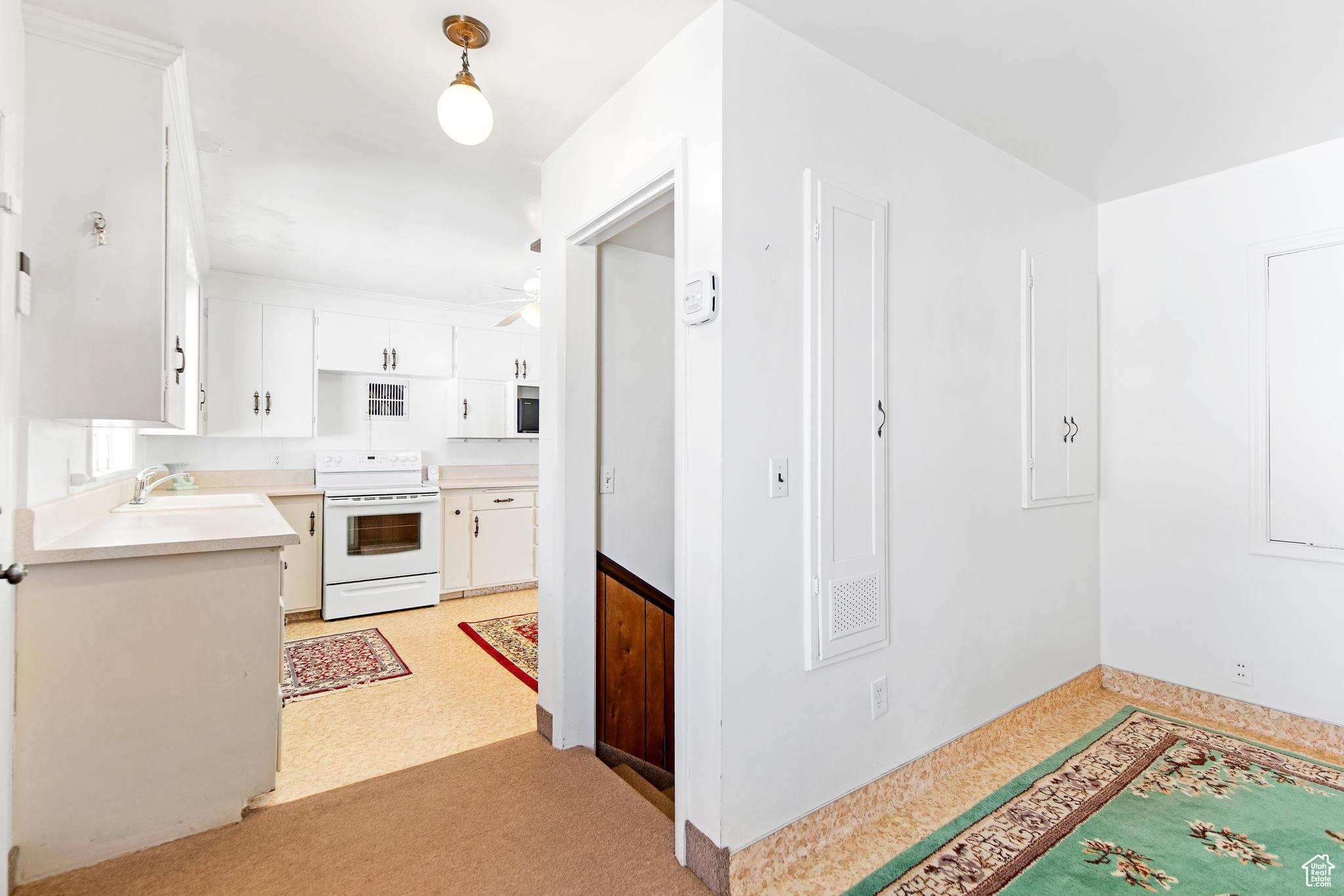 Kitchen with light countertops, electric range, white cabinetry, a ceiling fan, and a sink