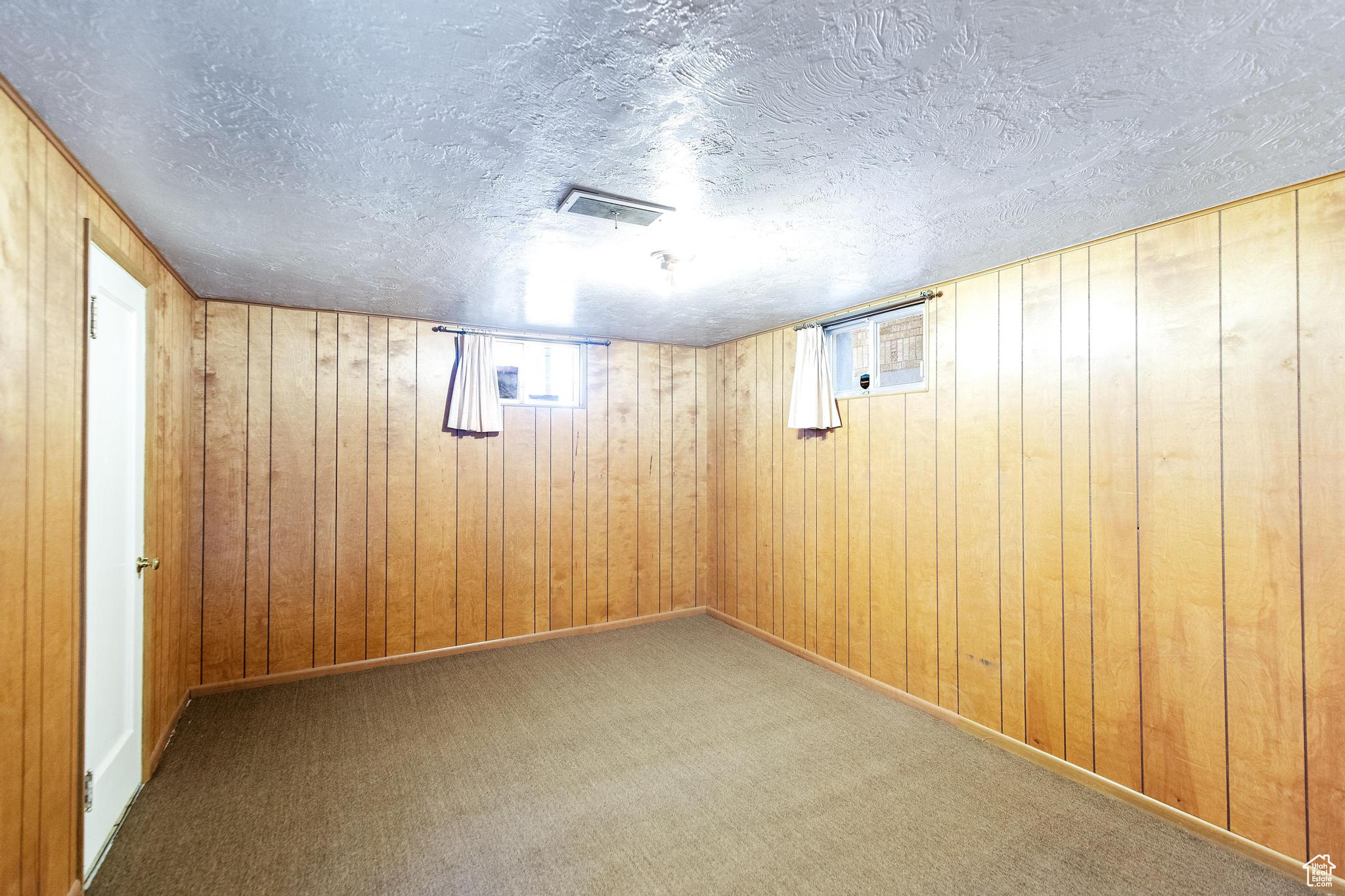 Basement featuring wooden walls, visible vents, a textured ceiling, and carpet