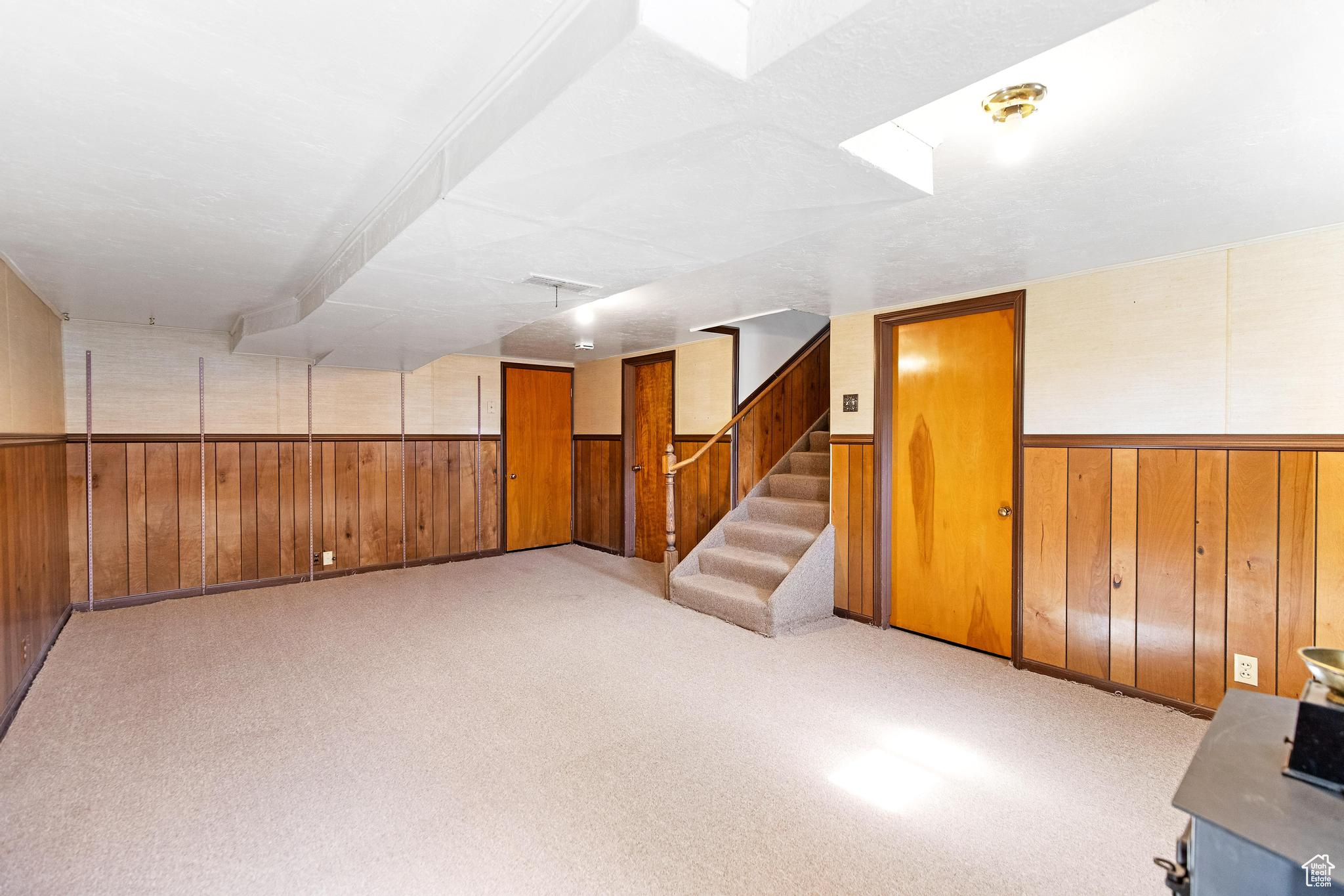 Basement with a wainscoted wall, light carpet, wood walls, and stairs