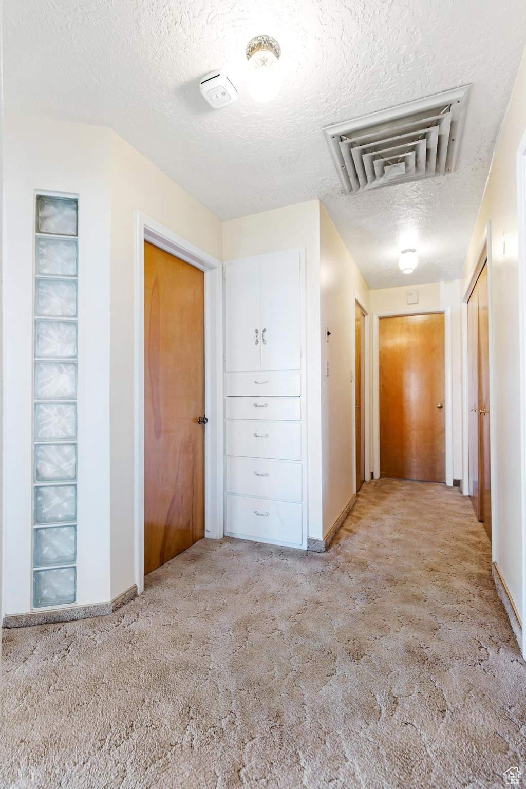 Hall featuring visible vents, baseboards, a textured ceiling, and carpet flooring