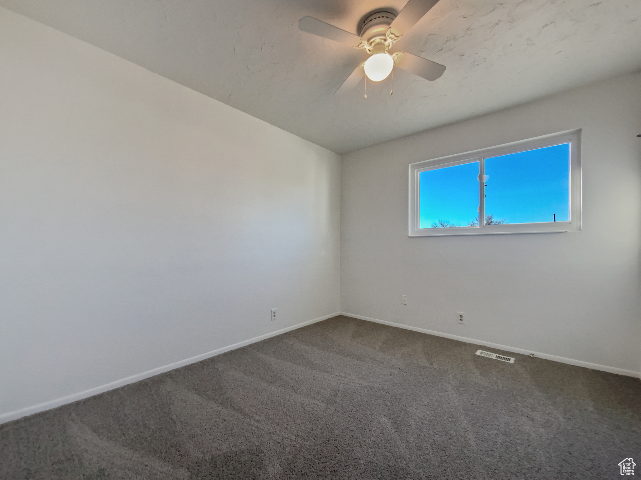 Unfurnished room featuring a ceiling fan, visible vents, dark colored carpet, and baseboards