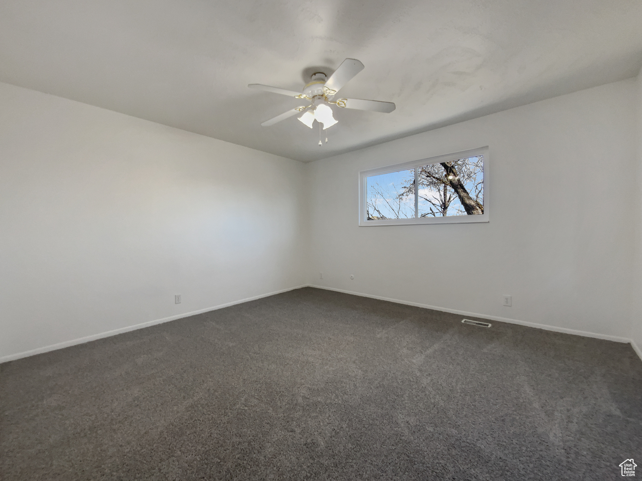 Empty room featuring dark colored carpet, visible vents, baseboards, and ceiling fan