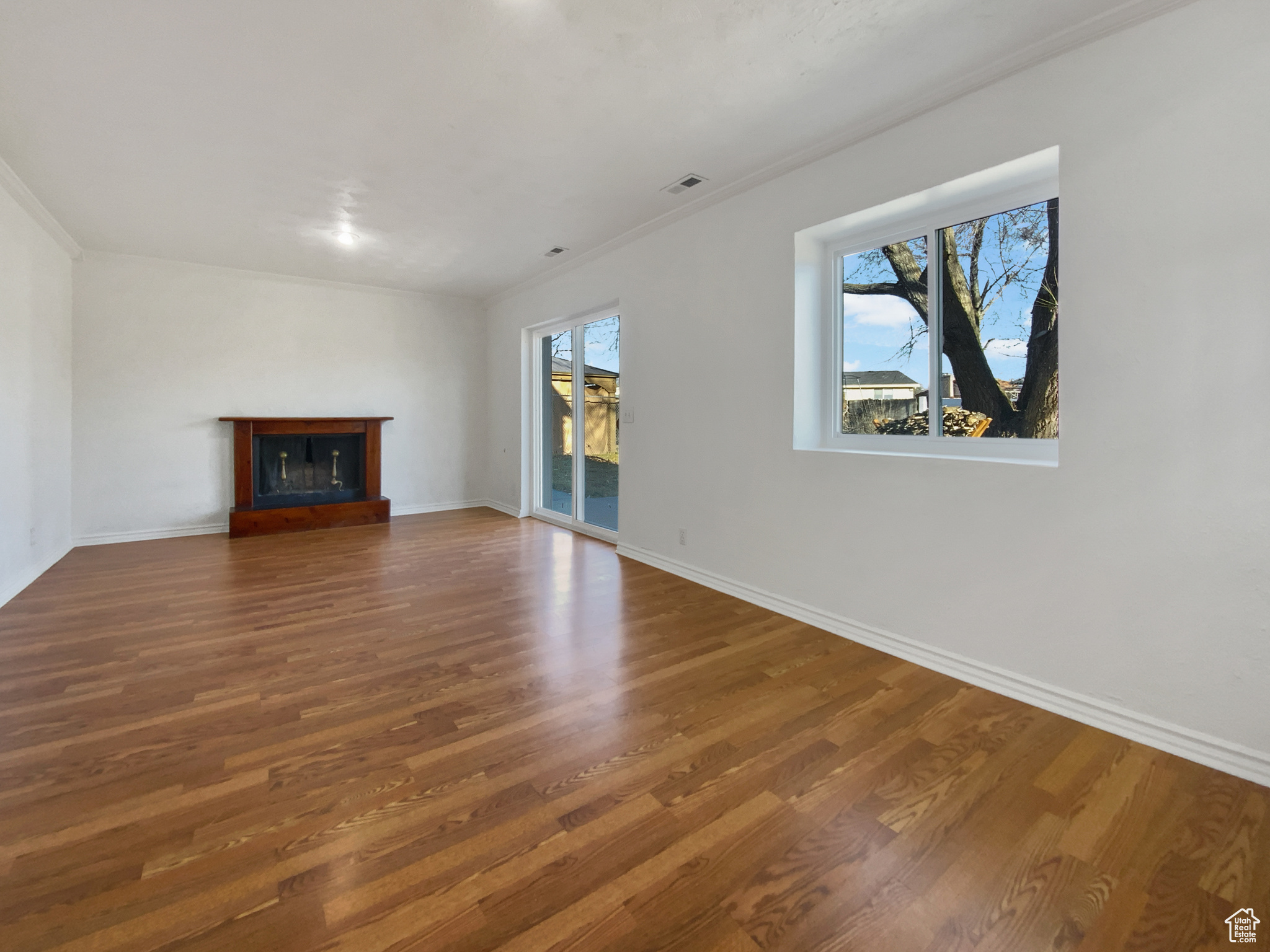 Unfurnished living room with visible vents, wood finished floors, a fireplace with raised hearth, and crown molding