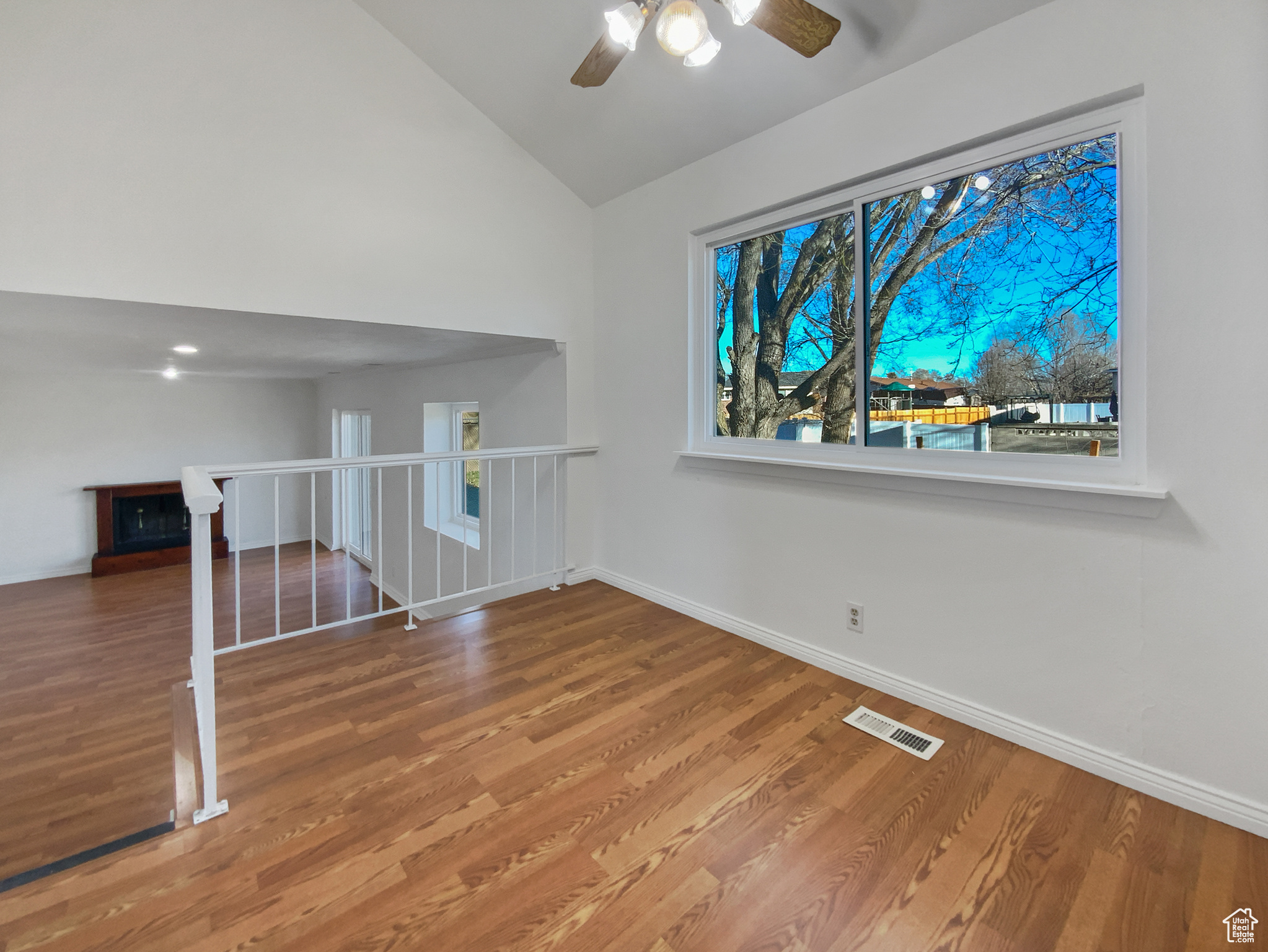 Empty room with vaulted ceiling, wood finished floors, visible vents, and baseboards