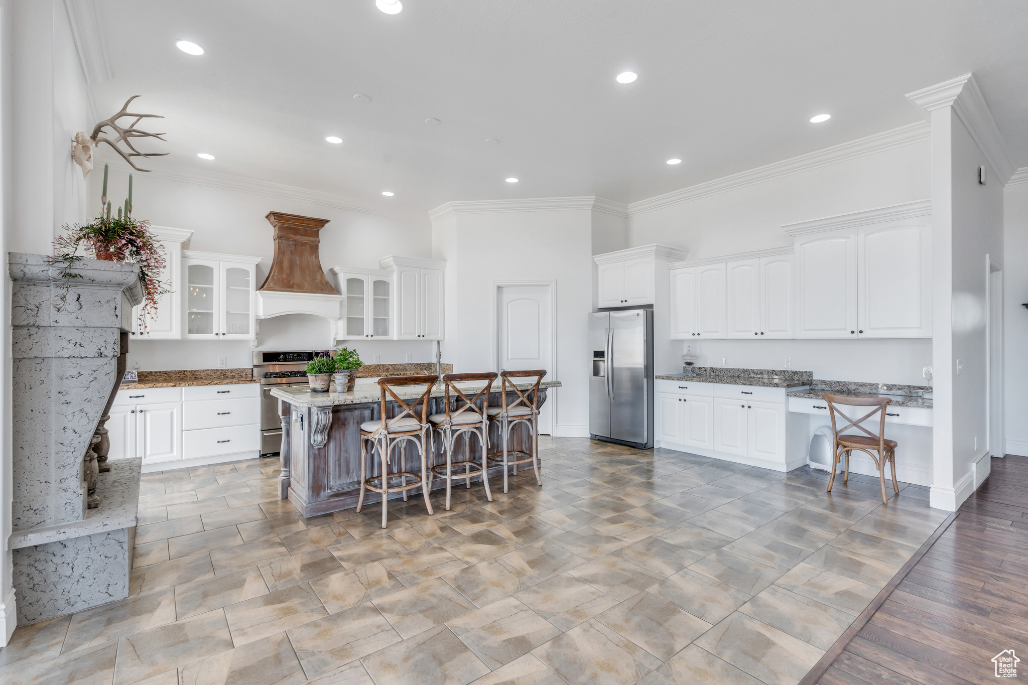 Kitchen featuring a breakfast bar, custom exhaust hood, white cabinets, and appliances with stainless steel finishes