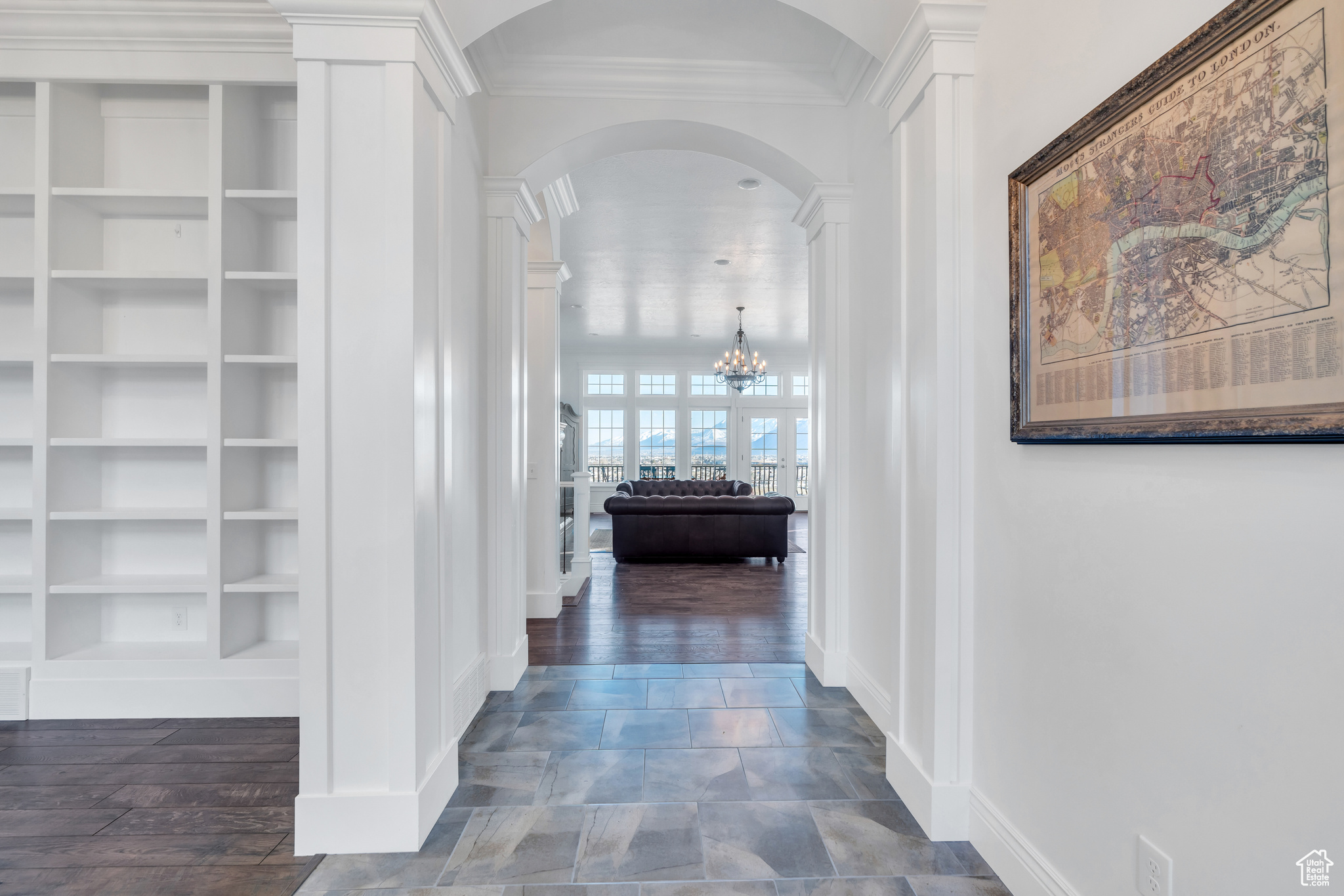 Corridor featuring built in shelves, arched walkways, ornamental molding, dark wood-type flooring, and a notable chandelier