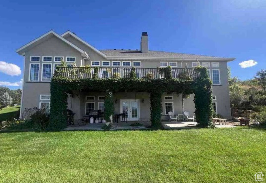 Back of house featuring a lawn, a deck, a patio, french doors, and a chimney