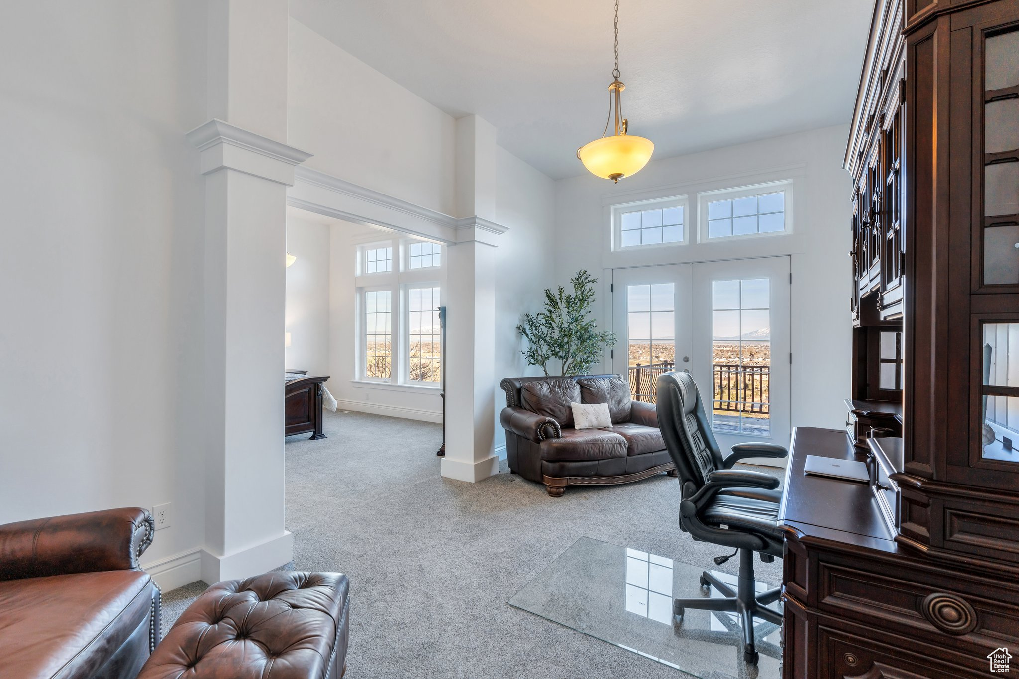 Carpeted office space featuring a towering ceiling, french doors, baseboards, and decorative columns