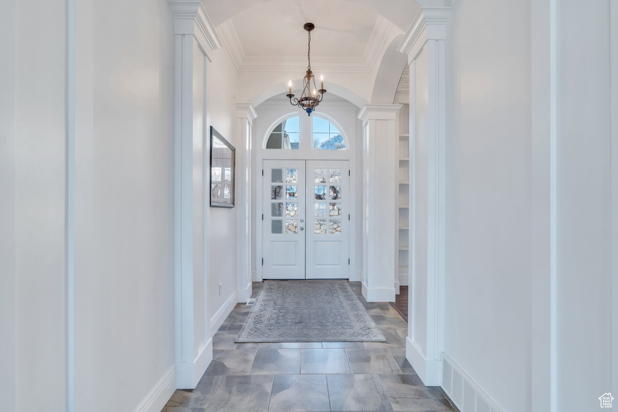 Entrance foyer featuring a chandelier, visible vents, arched walkways, and ornate columns