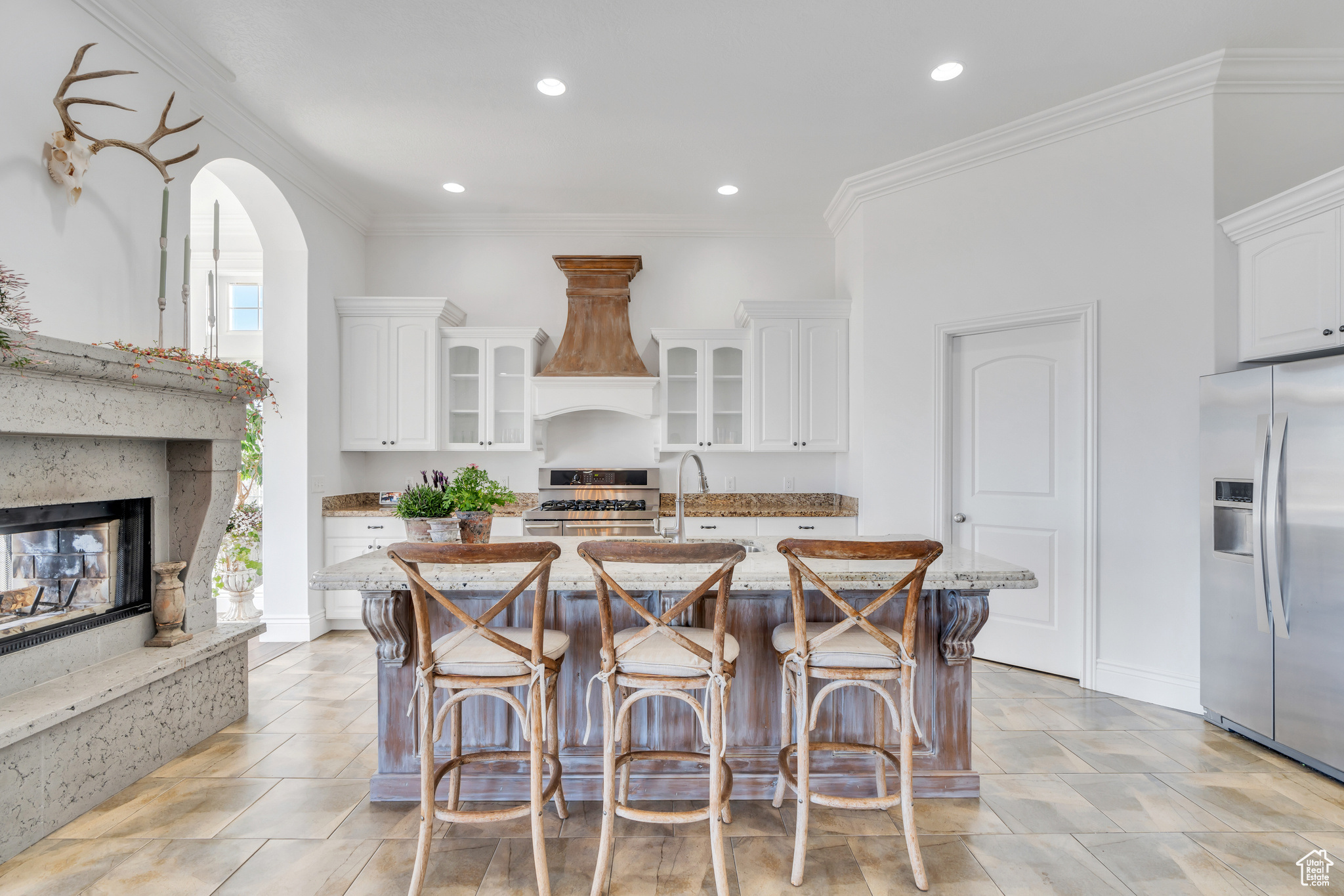 Kitchen with light stone counters, white cabinets, stainless steel appliances, and custom range hood