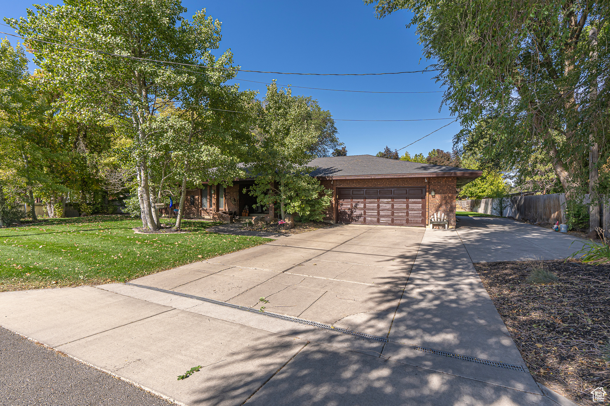 View of front of house featuring brick siding, fence, roof with shingles, a front yard, and driveway