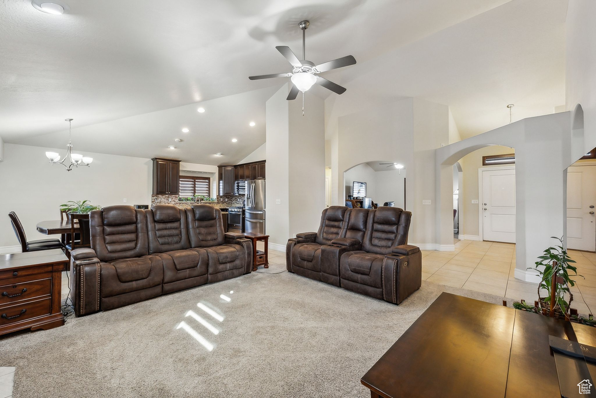 Living area with baseboards, high vaulted ceiling, light tile patterned flooring, arched walkways, and light carpet