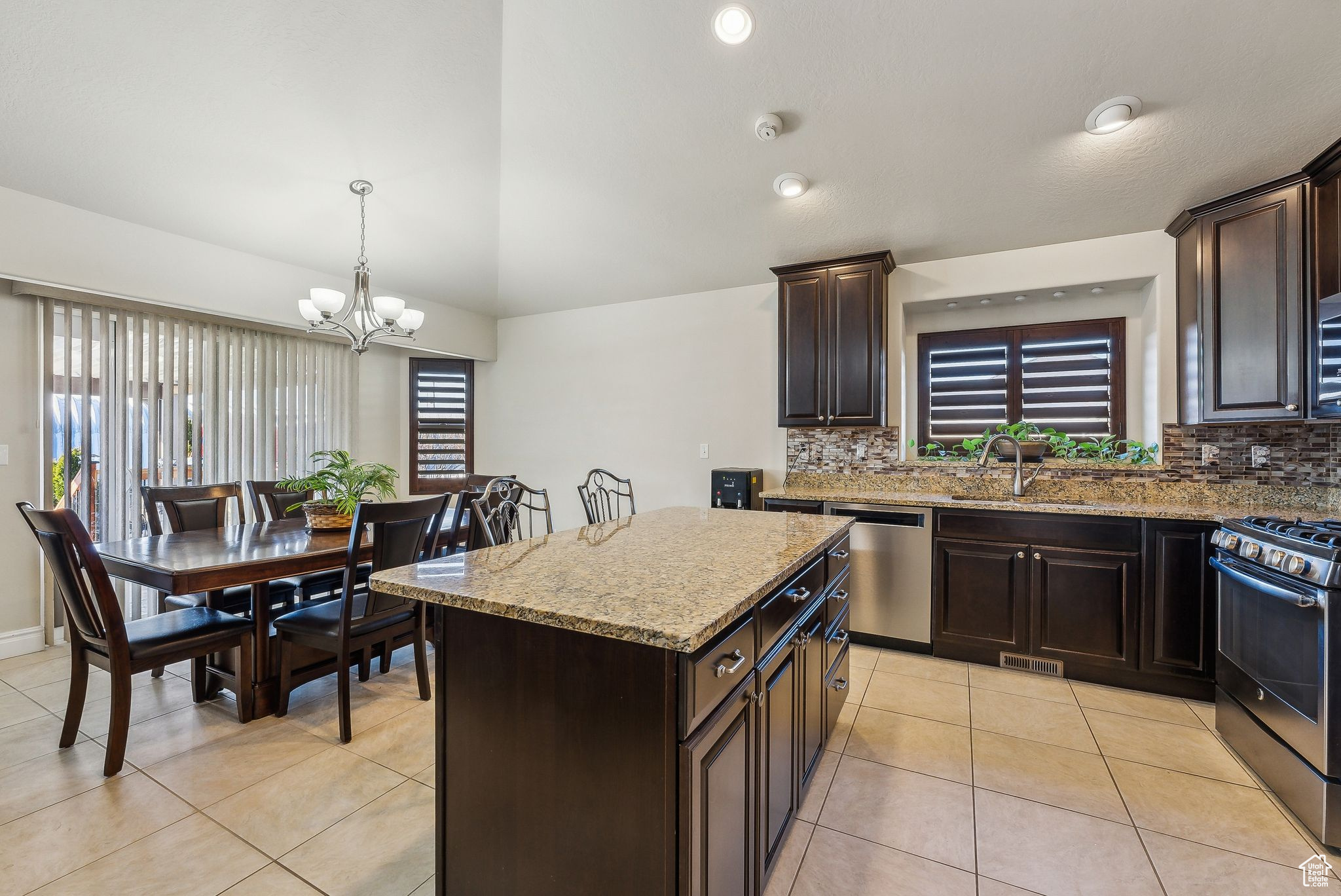 Kitchen with a sink, light stone counters, dark brown cabinetry, appliances with stainless steel finishes, and light tile patterned floors