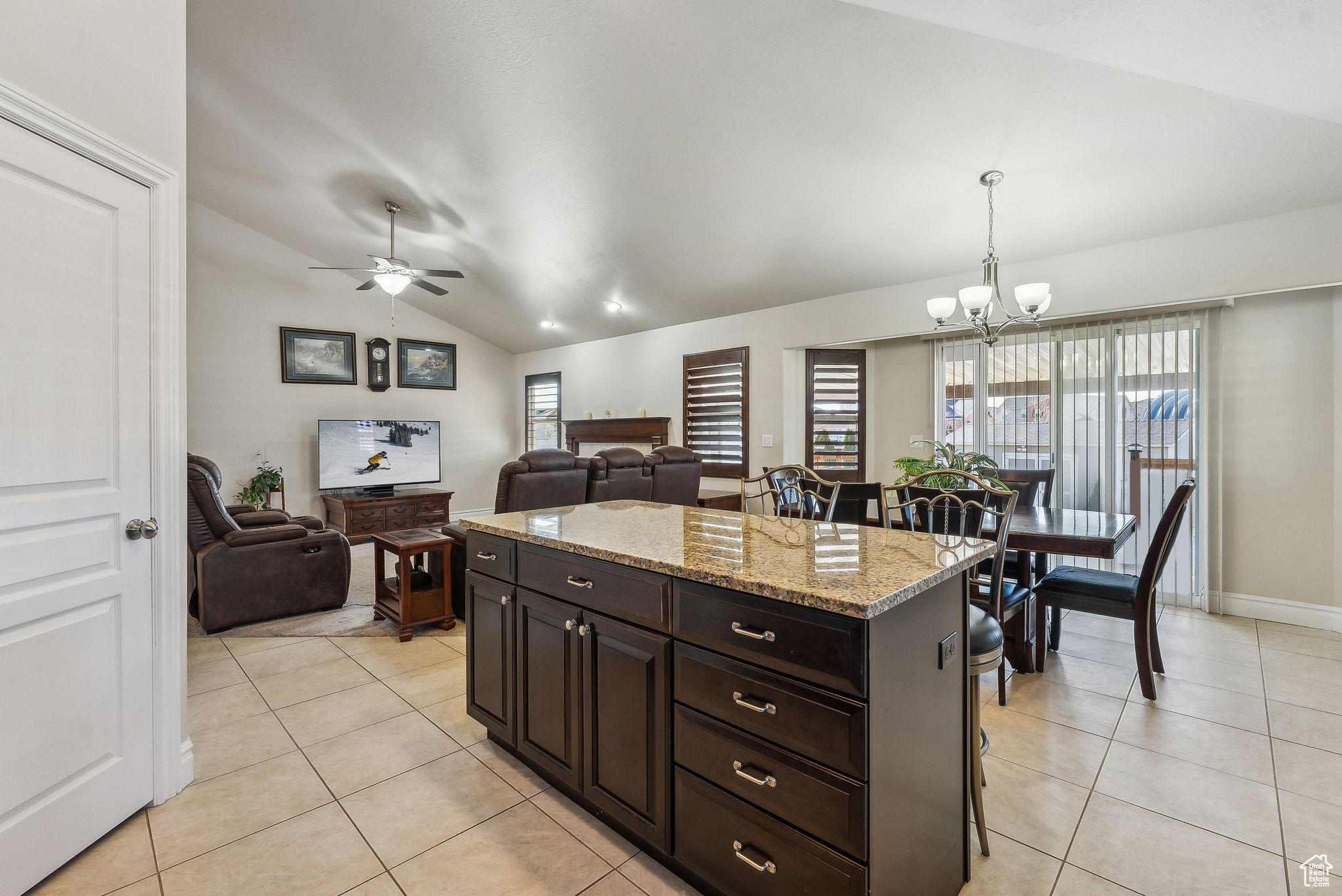 Kitchen with light tile patterned floors, light stone counters, ceiling fan with notable chandelier, and lofted ceiling