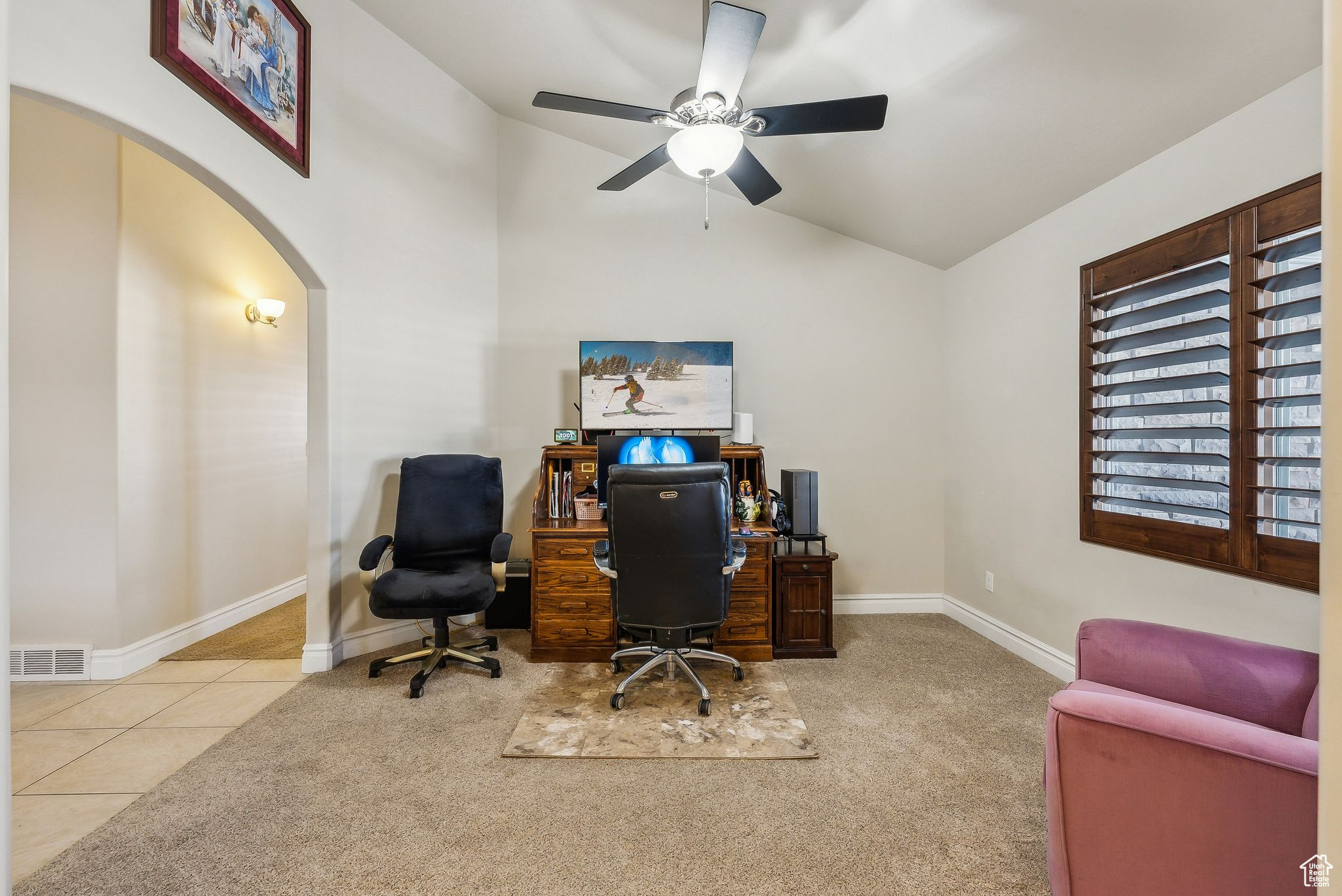 Carpeted home office with vaulted ceiling, visible vents, arched walkways, and baseboards